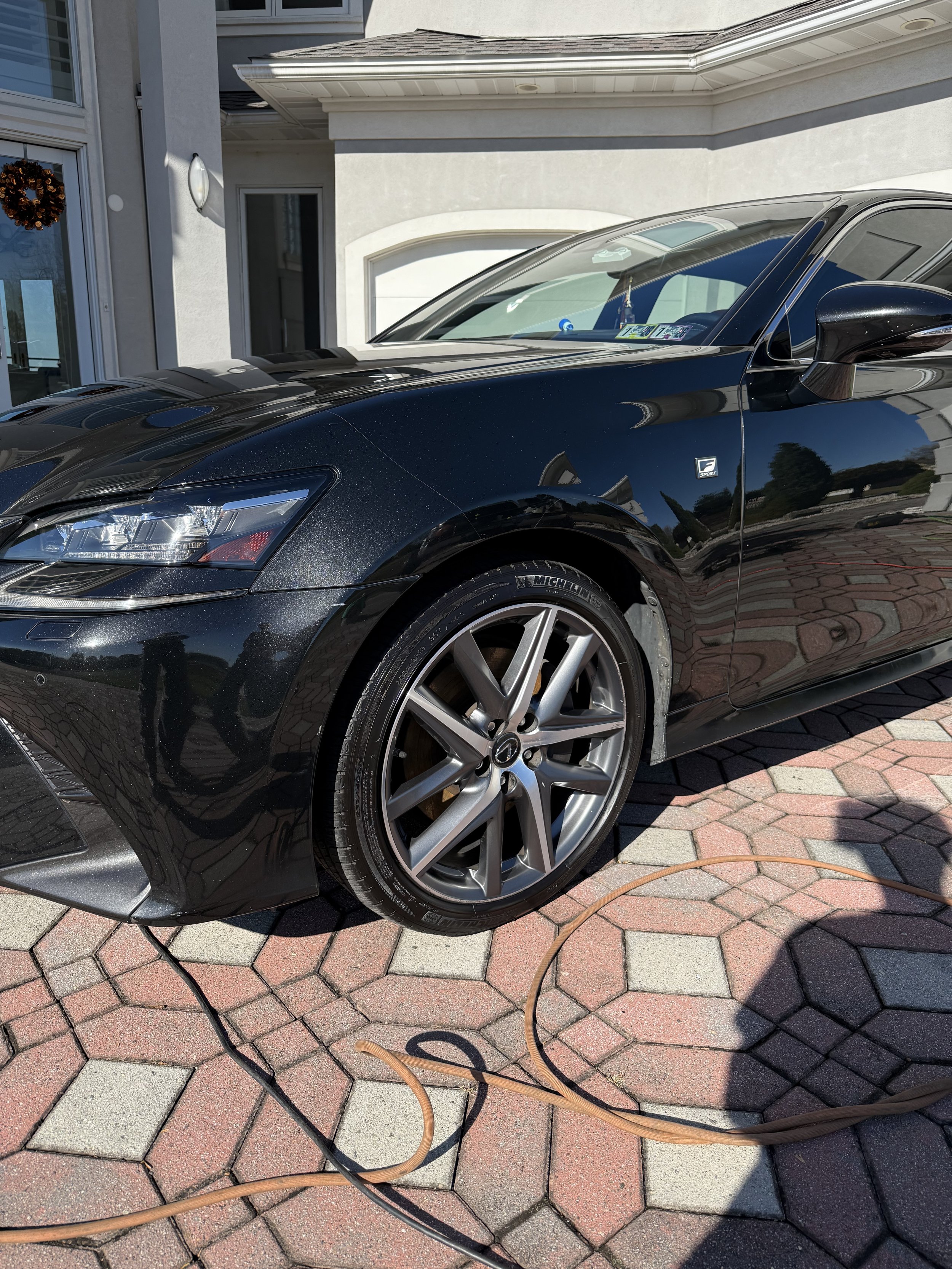 Black luxury car parked on a brick driveway in front of a white house exterior.