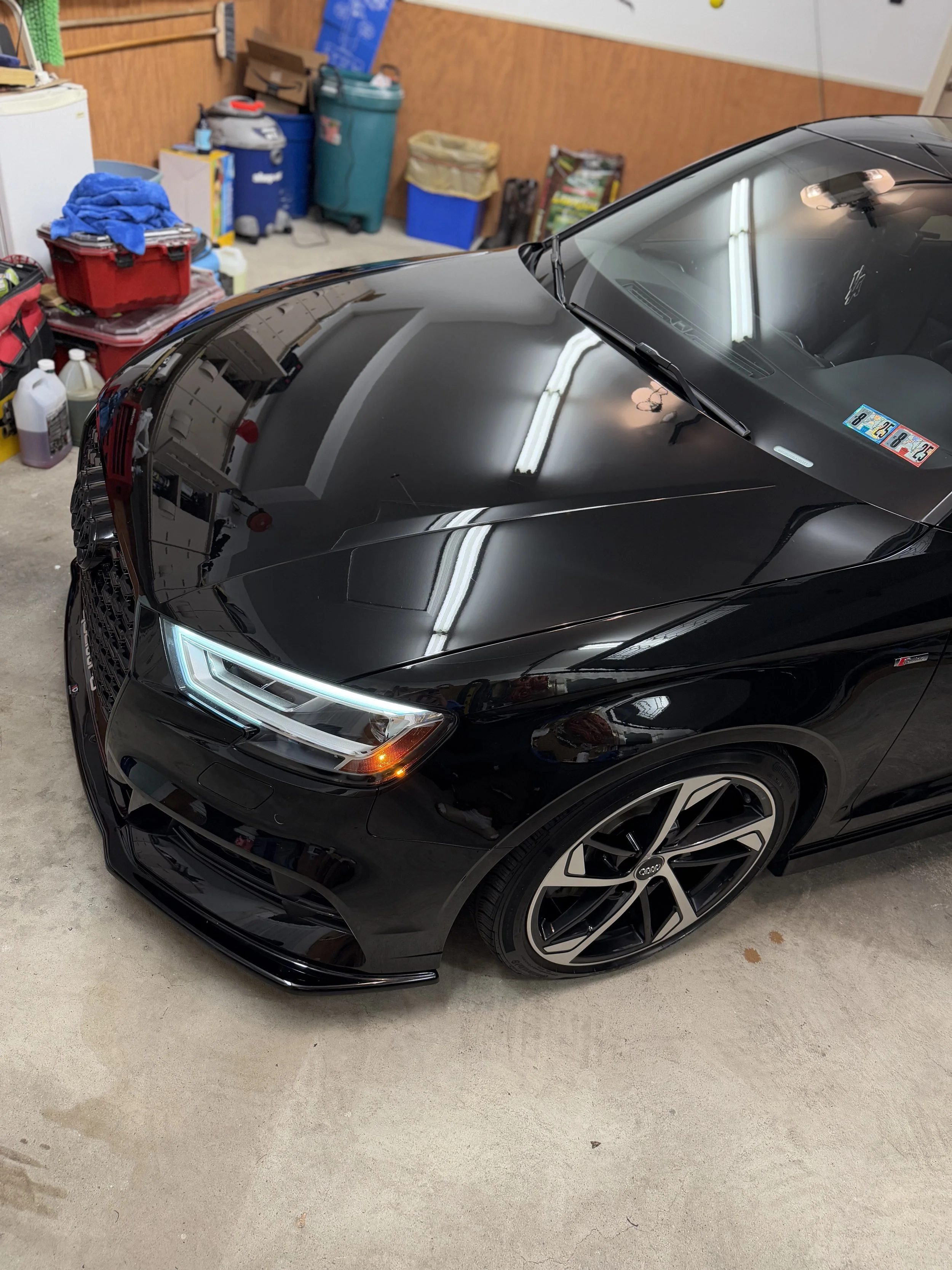 Black Audi car parked inside a garage with various tools and storage boxes in the background.