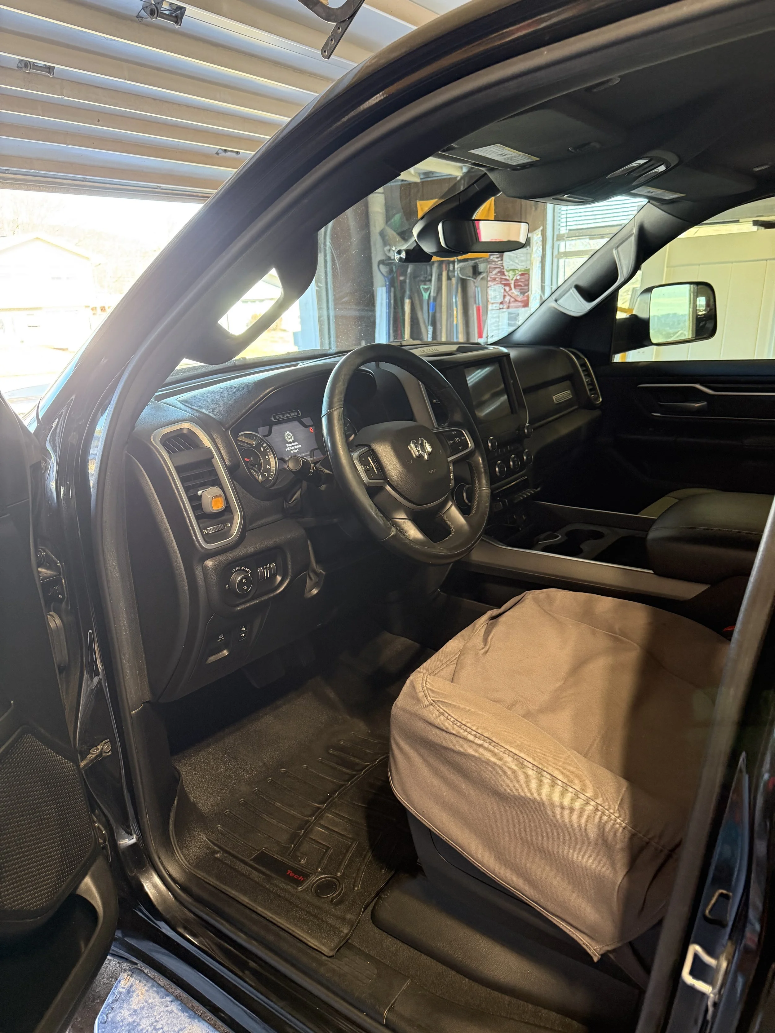 Interior of a pickup truck showing the driver's seat, dashboard with steering wheel, and various controls. The passenger seat is covered with a beige cloth, and a glove compartment is visible.