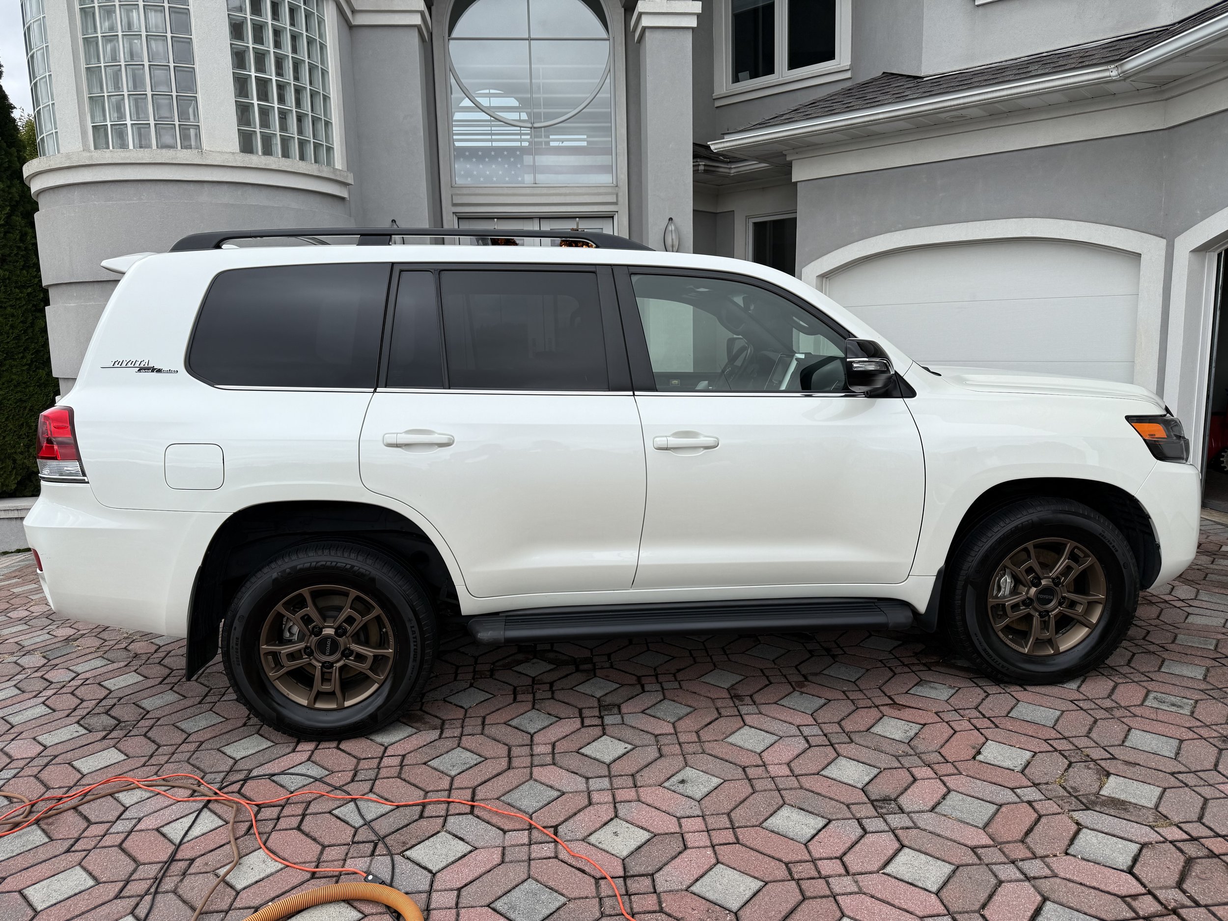 White SUV parked in front of a house with a grey and white exterior, driveway paved with interlocking bricks, and an extension cord on the ground.