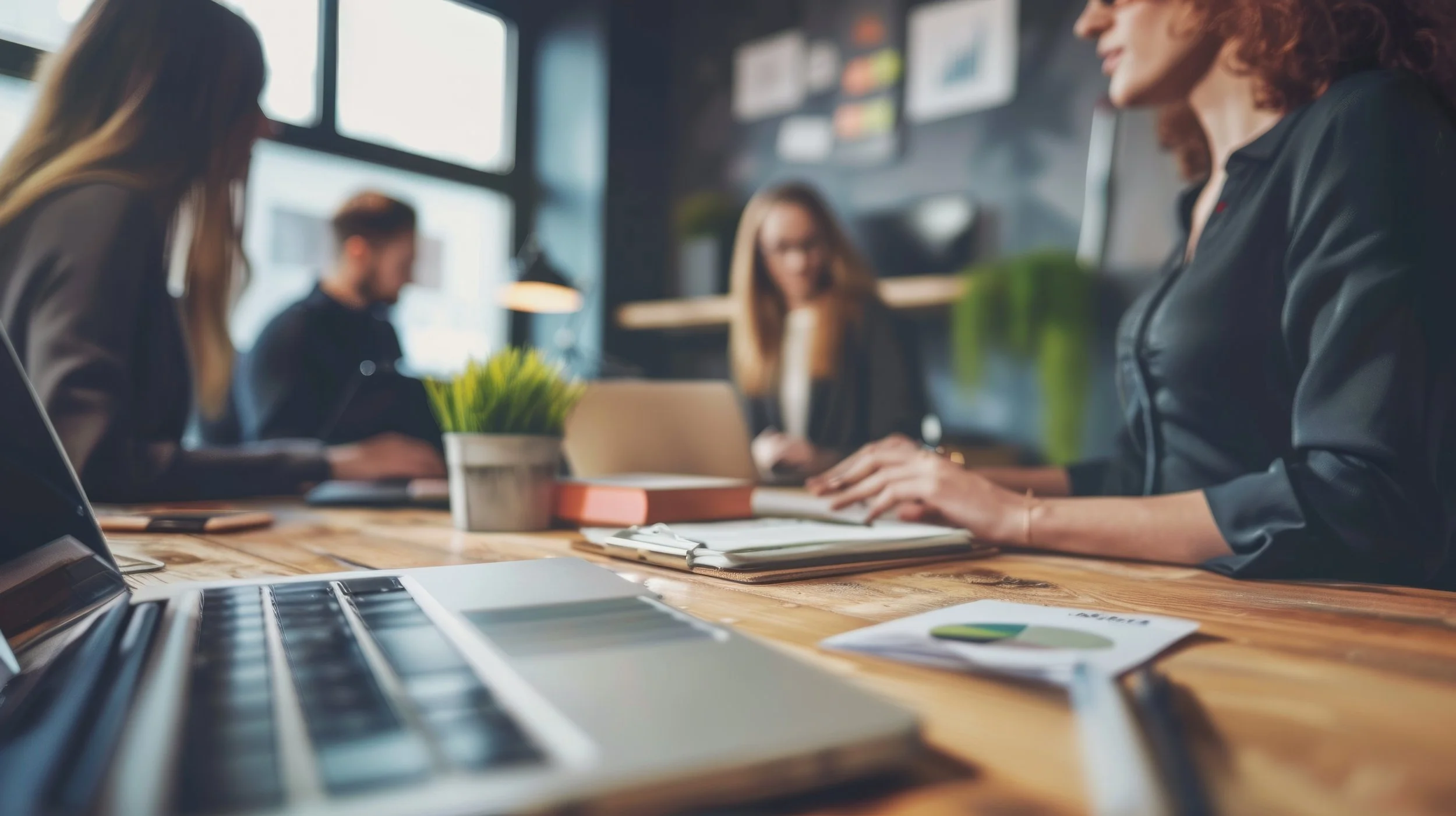 Diverse professional business team collaborating on digital program around conference table with laptops, charts, and notes in a modern office meeting