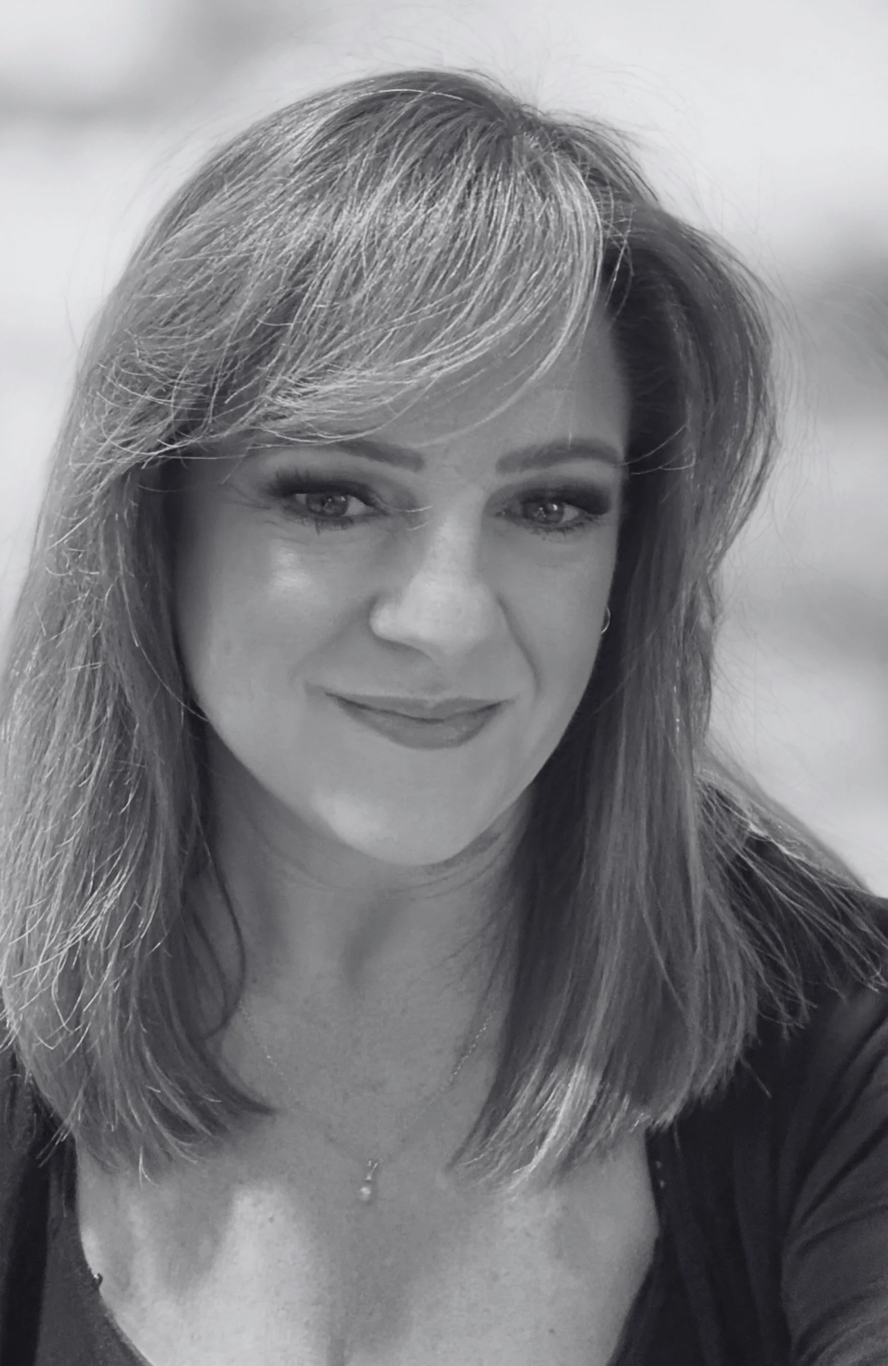 Black and white portrait of a woman with shoulder-length hair, smiling, wearing a top and a necklace.