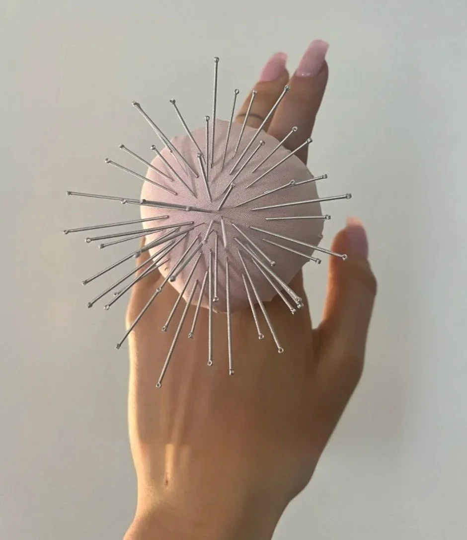 Main tenant une tomate de couture en tissu rose avec plusieurs aiguilles d'acupuncture
