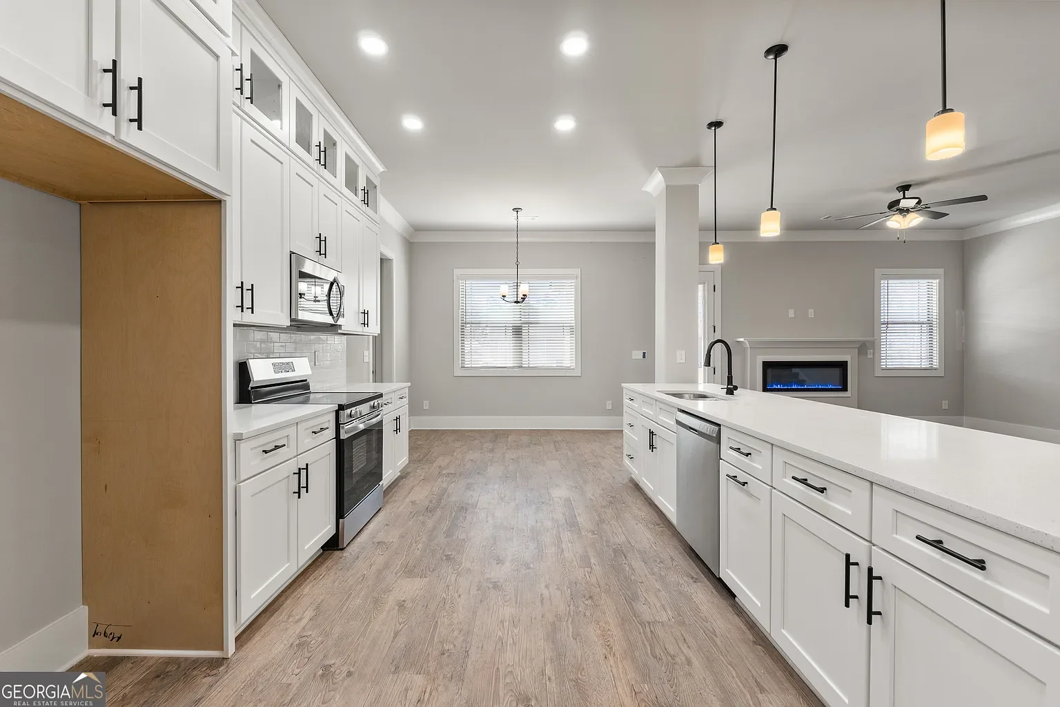 Modern kitchen with white cabinets, stainless steel appliances, a large island with a sink, pendant lighting, and a living area with a fireplace
