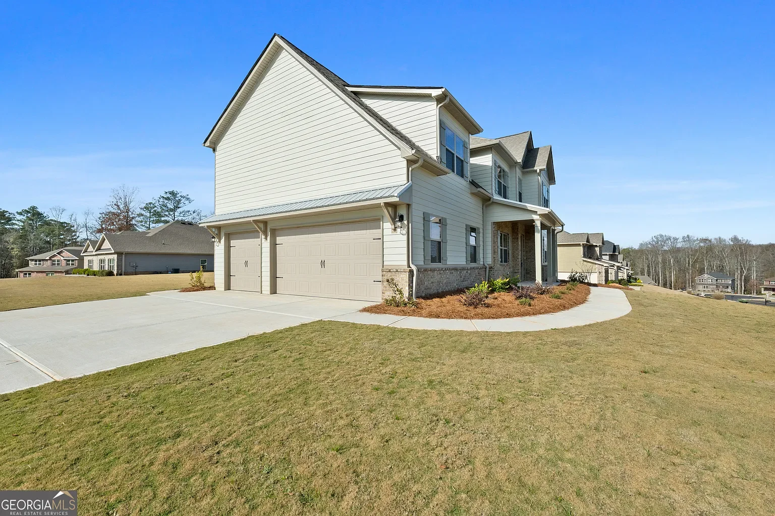 Front view of a two-story beige house with a garage and a landscaped yard under a clear blue sky.