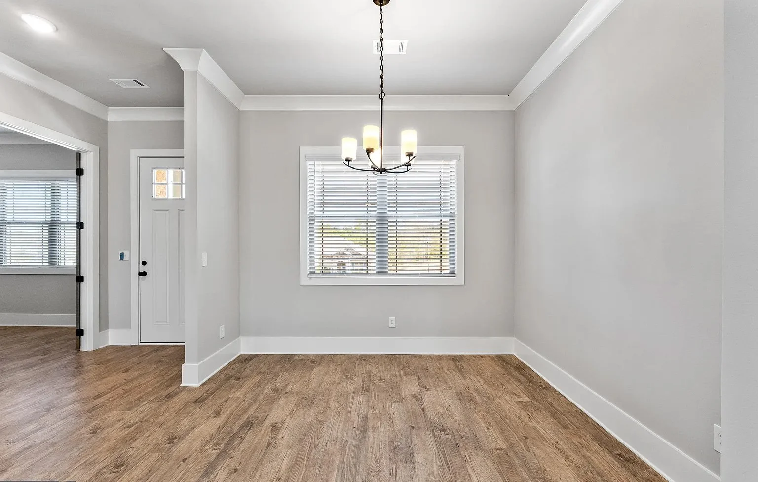 Empty dining room with a window, chandelier, and hardwood flooring.