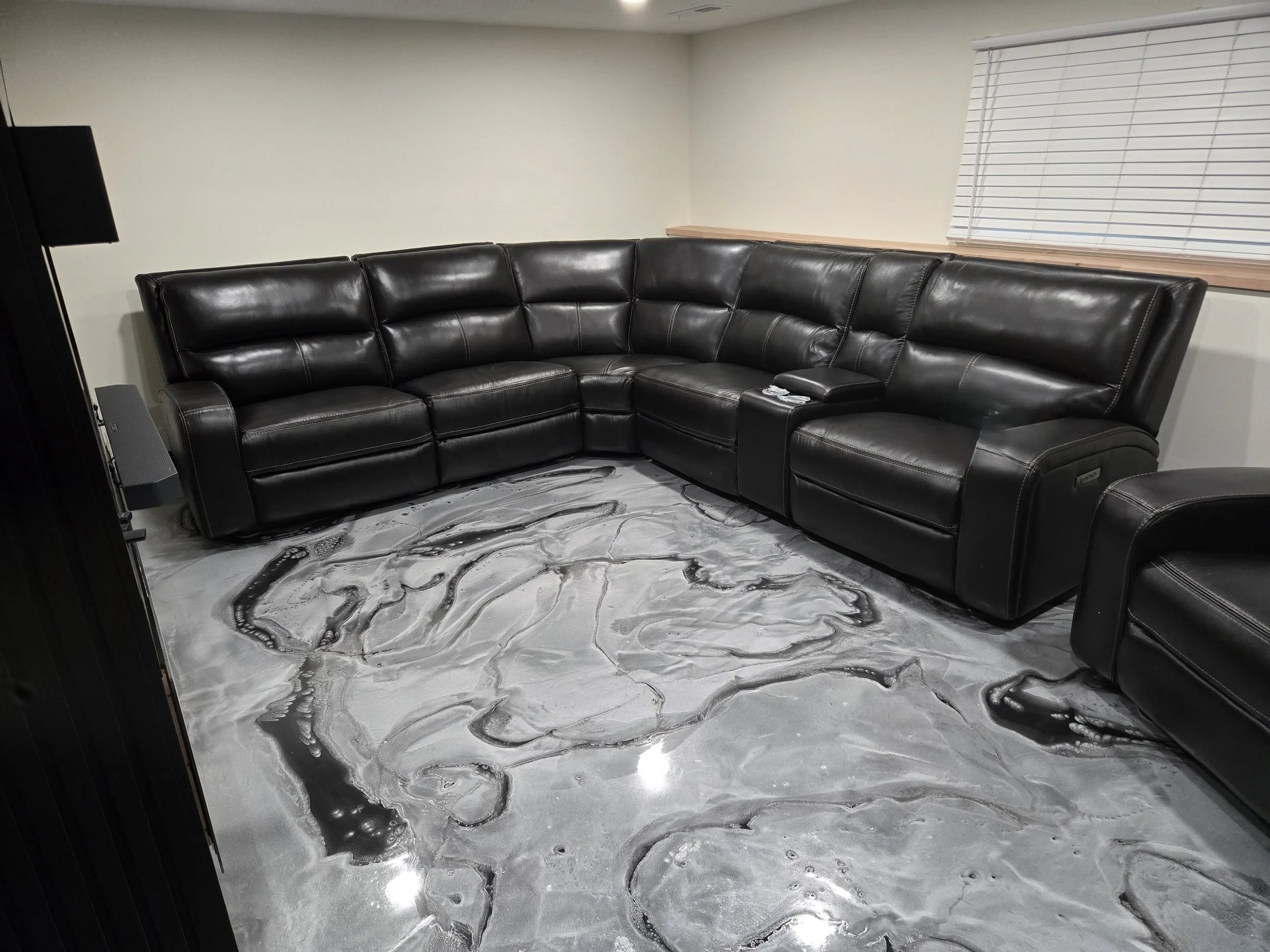 A black leather sectional sofa in a living room with a metallic epoxy floor.