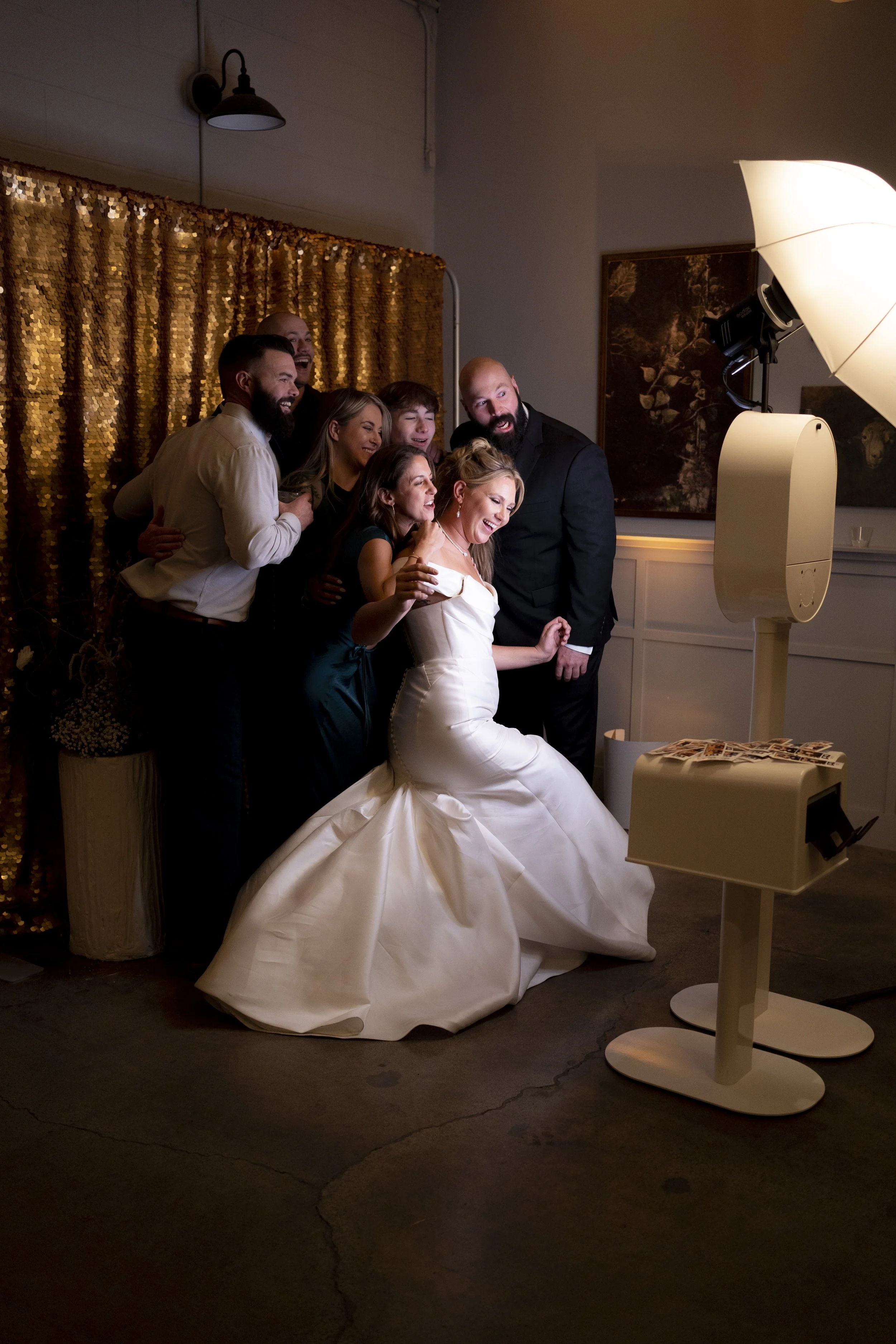 A group of people taking a photo of a bride in her wedding dress in a photo booth at a wedding reception.