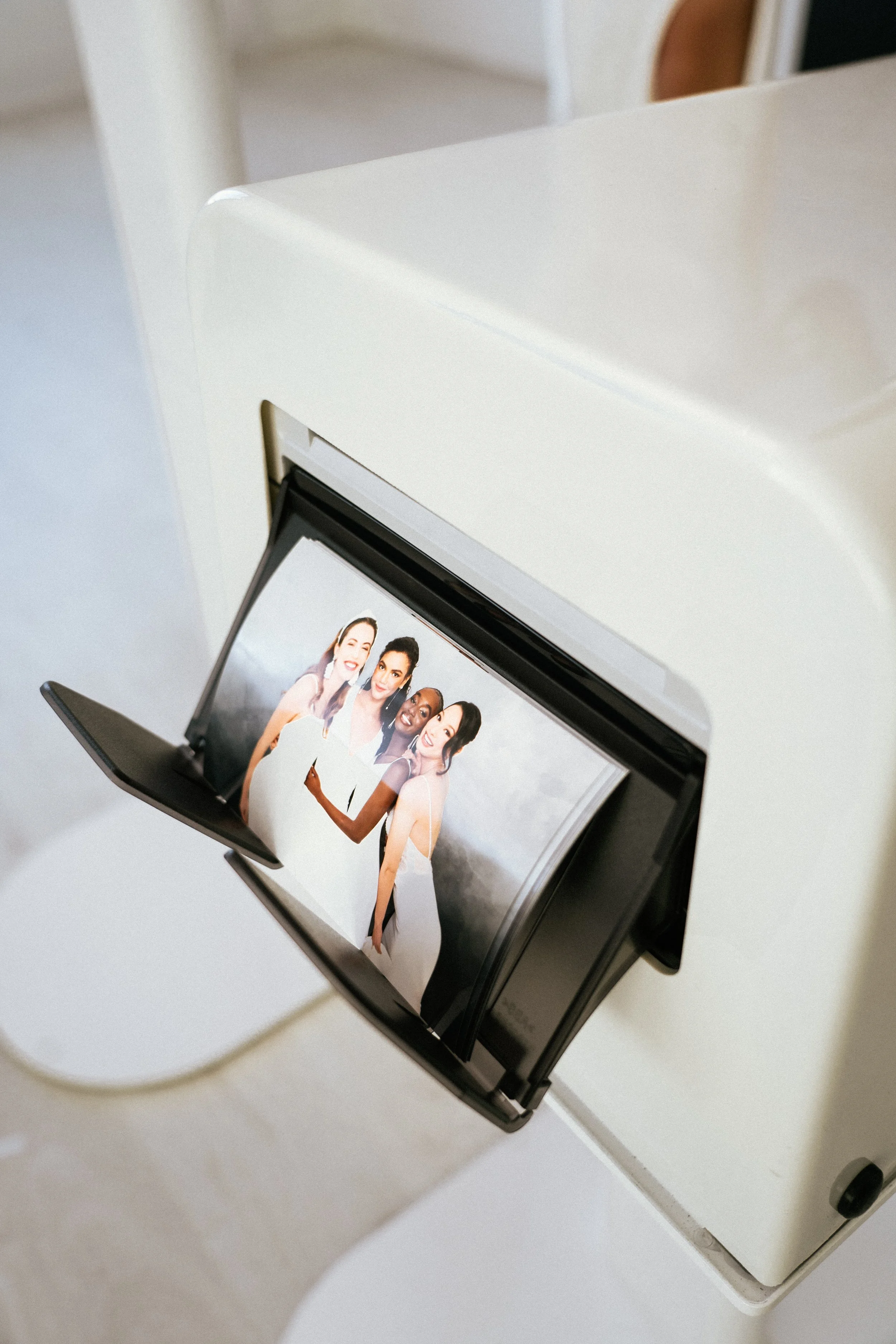 Photo booth displaying a picture of four women smiling, dressed in white, with two wearing wedding dresses.