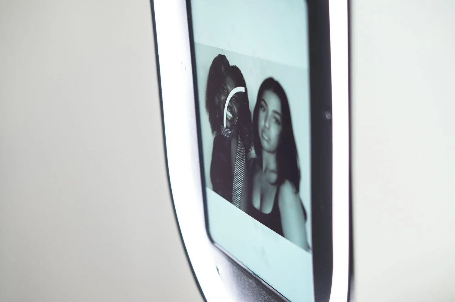 close-up of a digital camera screen displaying a photo of two women, one with curly hair and the other with straight hair, both smiling and posing for a selfie.