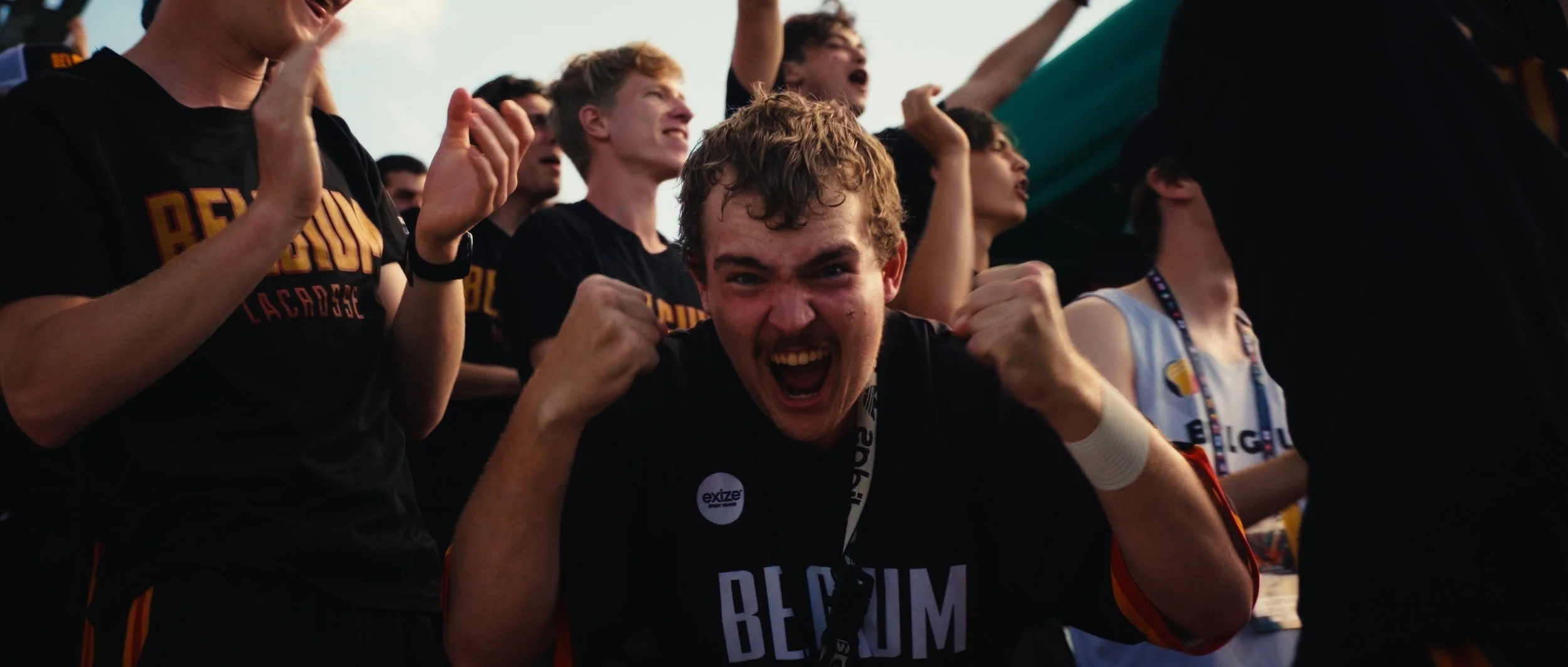 Group of lacrosse players celebrating, with one in the foreground enthusiastically cheering and clenching fists.