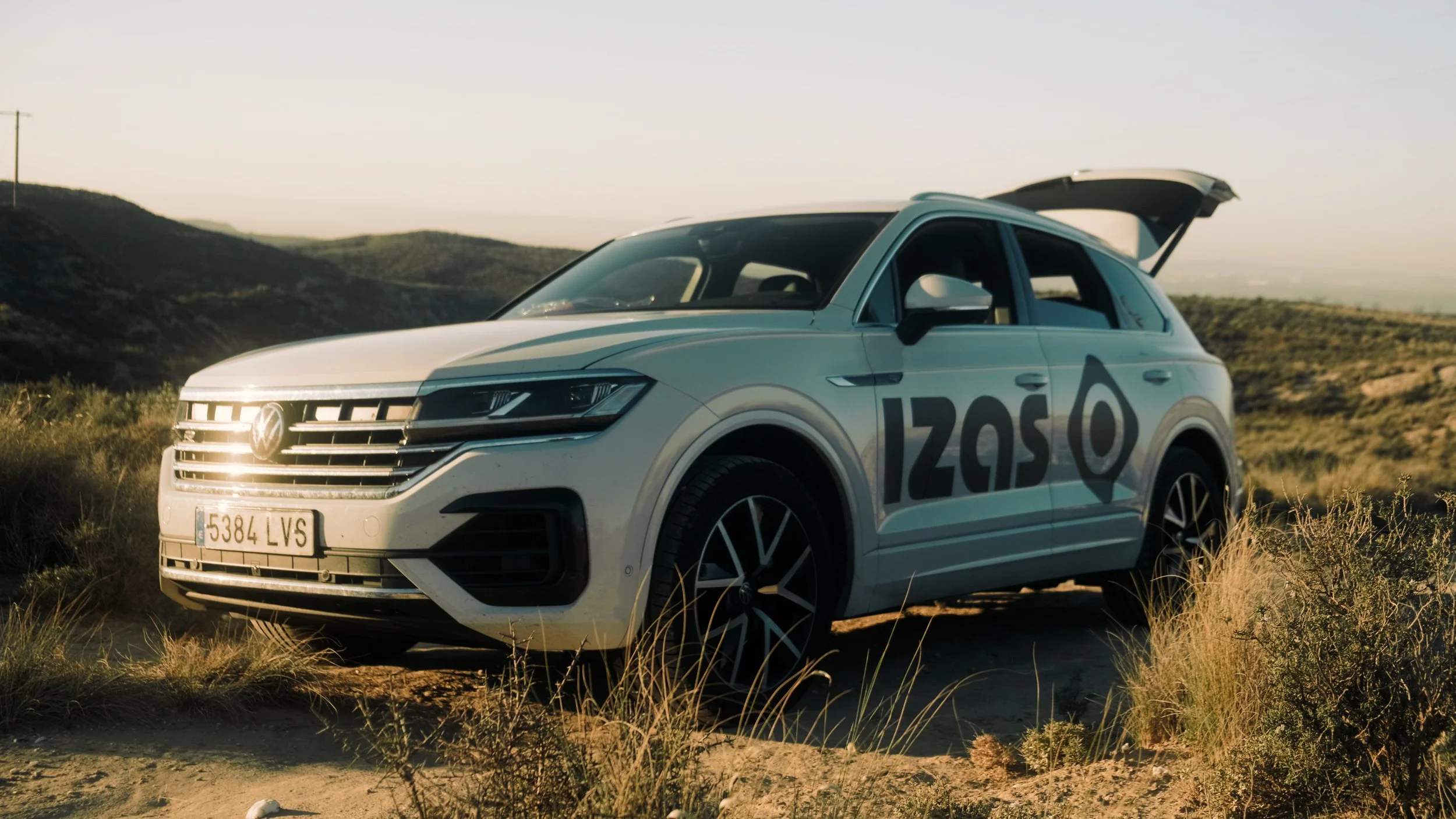 A white Volkswagen ID.5 electric SUV parked on a grassy hillside with mountains in the background during sunset.