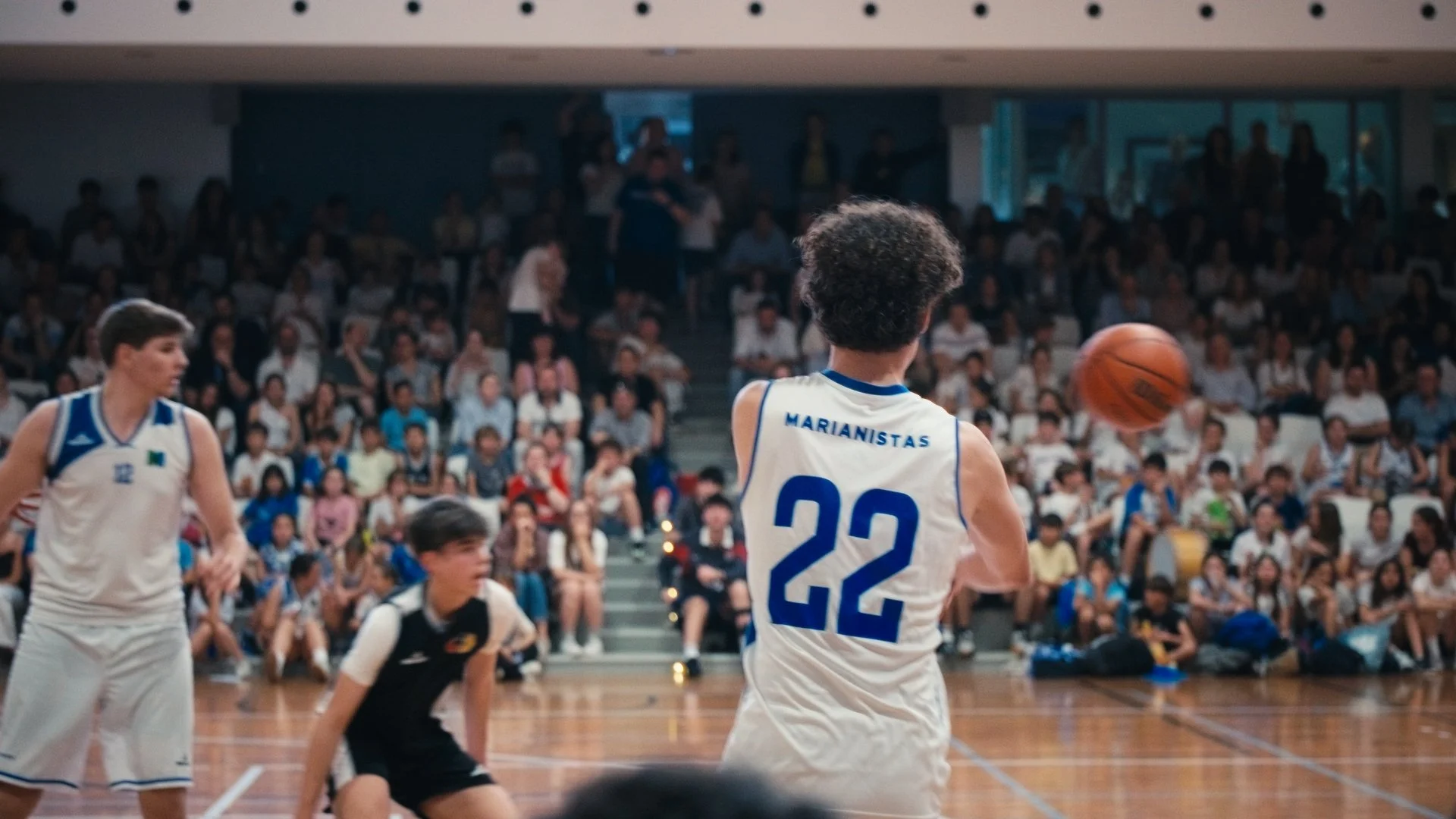 A basketball game in progress with players on the court and spectators in the stands, including a player wearing a white jersey with the number 22.