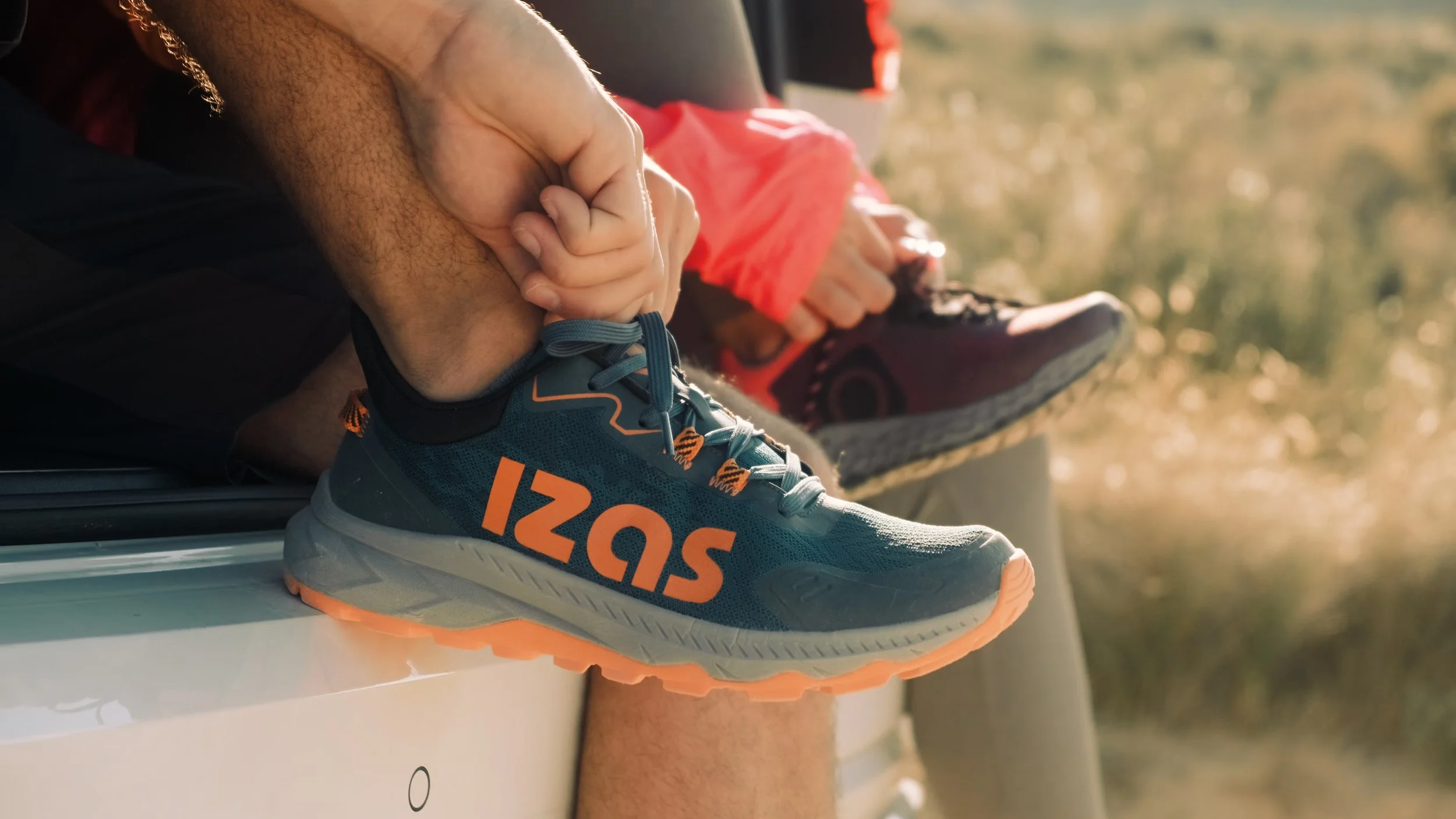 Close-up of a person's foot in a running shoe, with a hand gently holding the ankle. The shoe has the number 5296 on it, and the background shows a blurred outdoor setting.