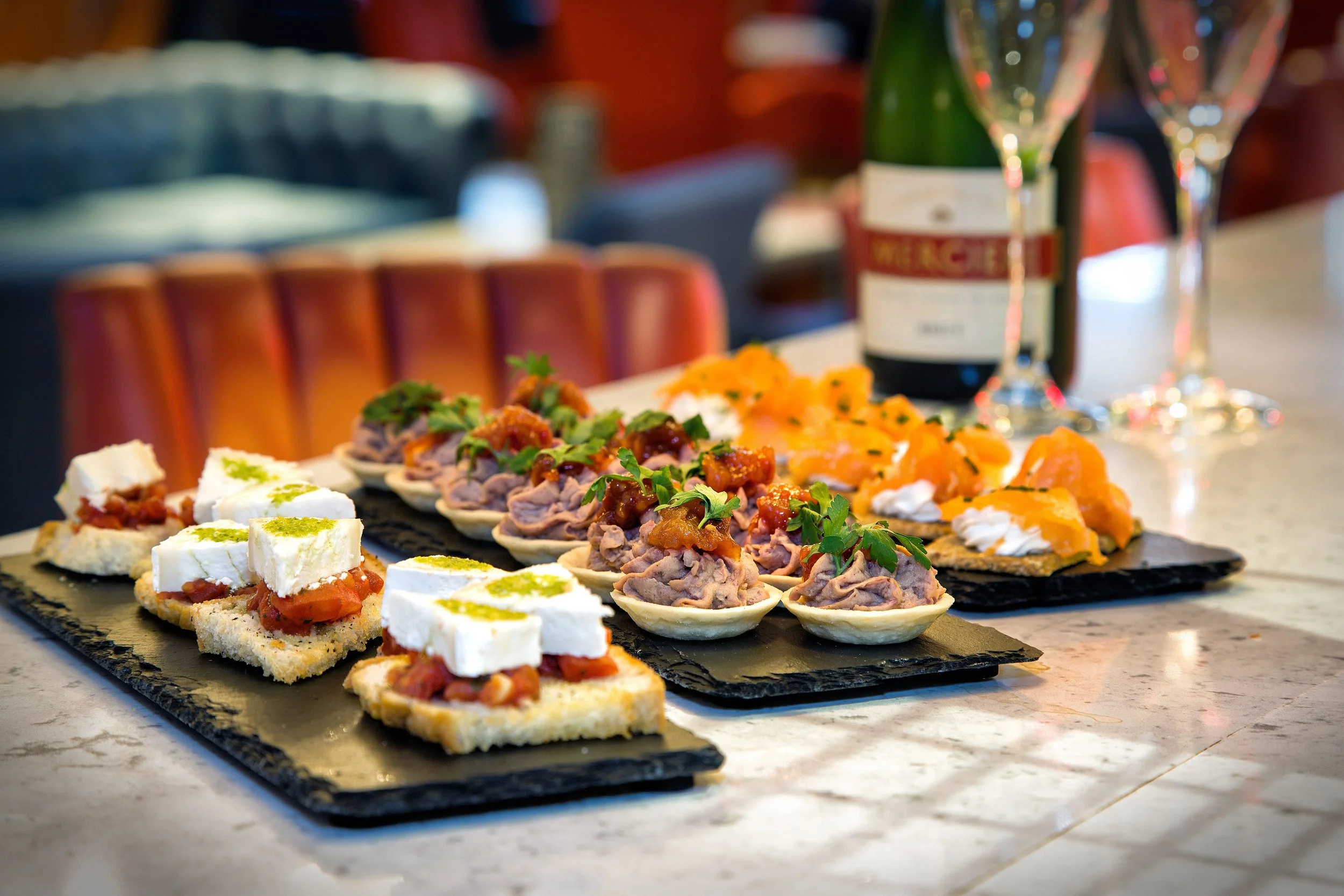 Variety of appetizers on black slate serving boards, with a bottle of champagne and glasses in the background