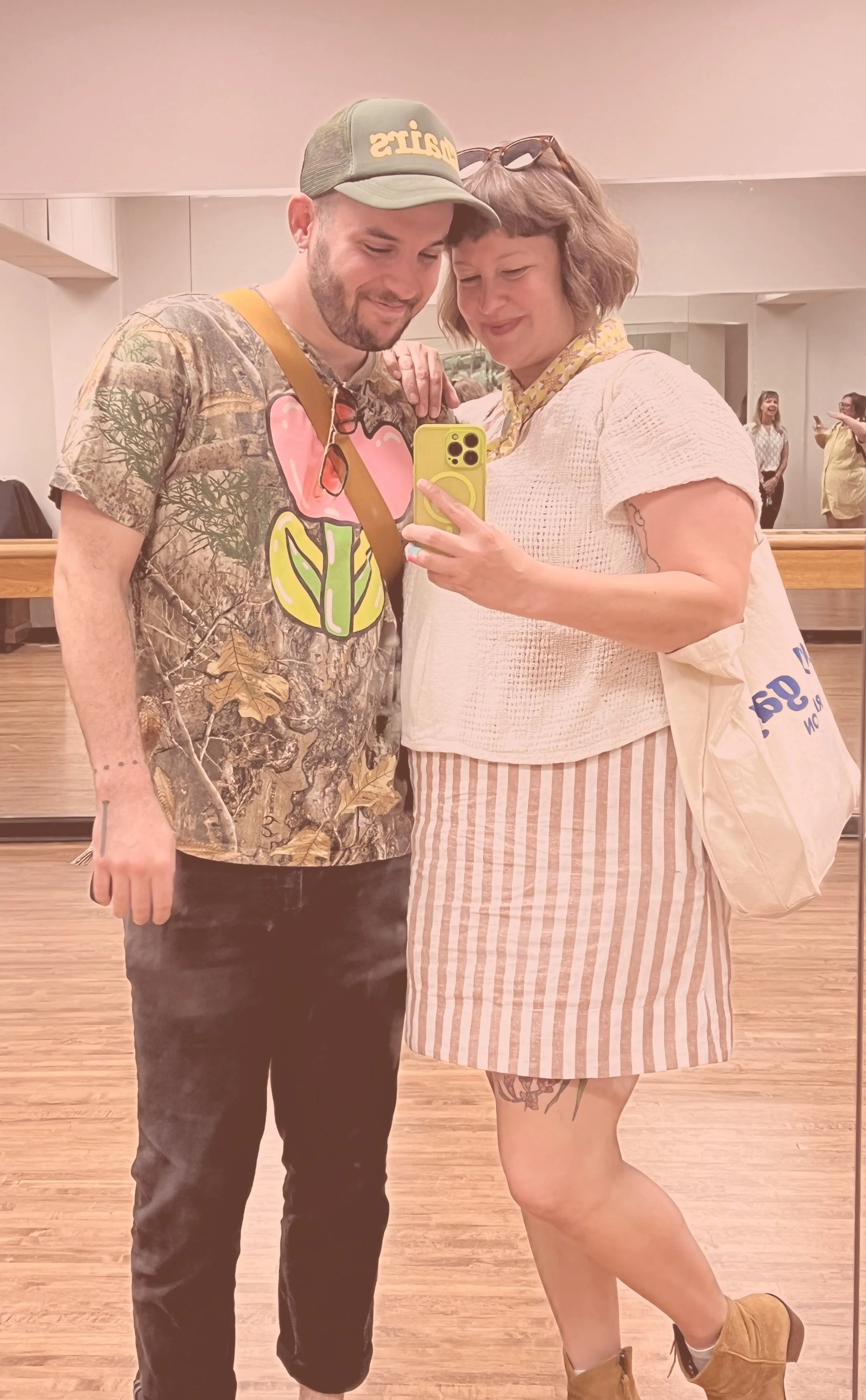 A non-binary person and a woman taking a selfie together in a ballet studio mirror
