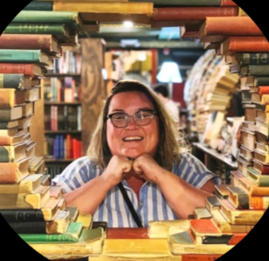 A woman with dark skin smiles with her chin in her hands and peers through a portal of books