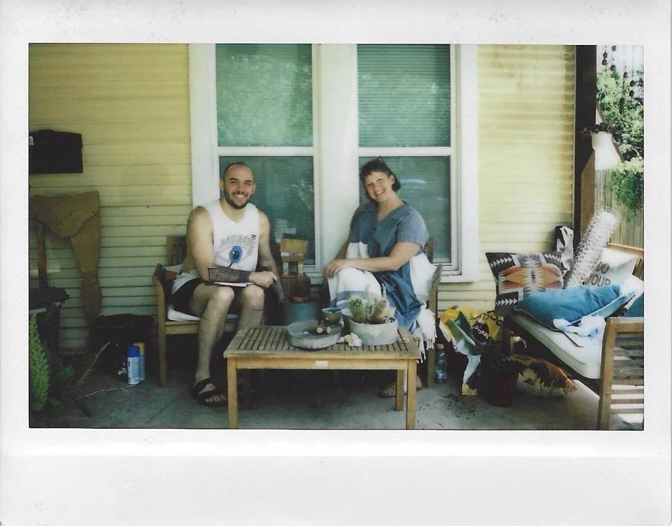 a scanned polaroid of two people sitting on a porch surrounded by cacti and wooden sculptures
