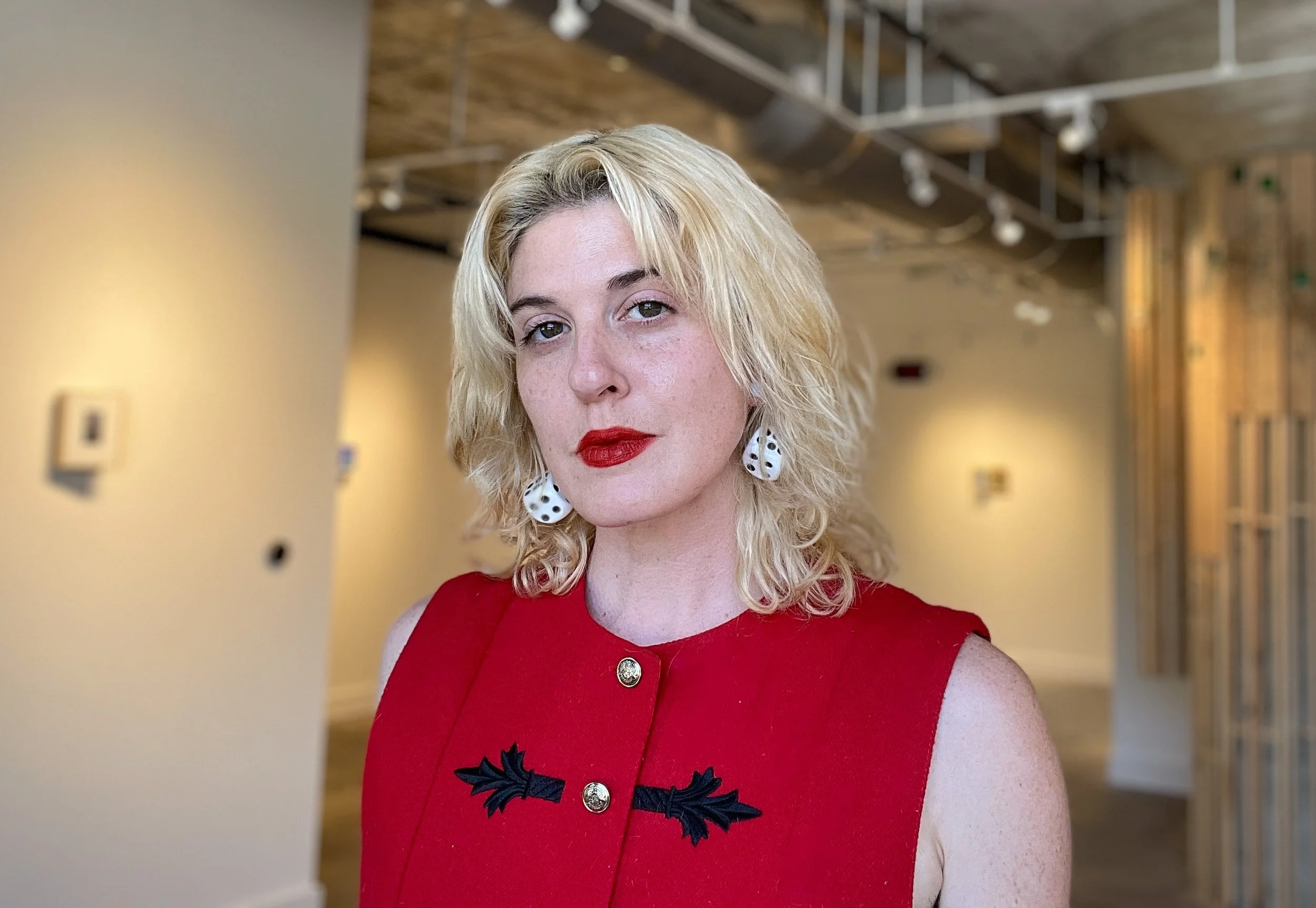 A non-binary person with light skin and red lipstick stands in a gallery