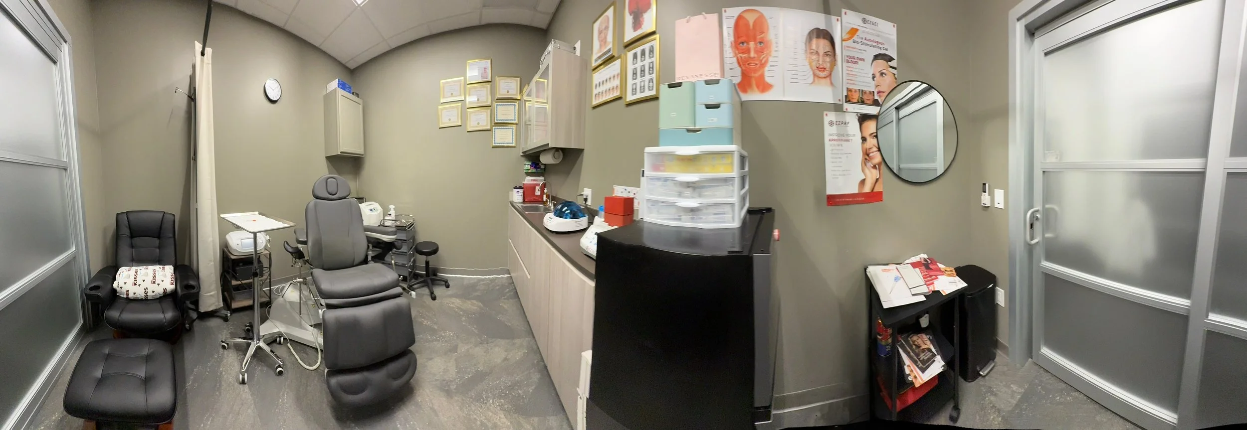 A medical consultation room with chairs, medical equipment, and posters about skin care and facial anatomy on beige walls.