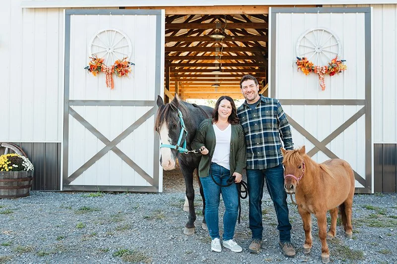 April and Bryan with Ritz and Cupid in front of white barn