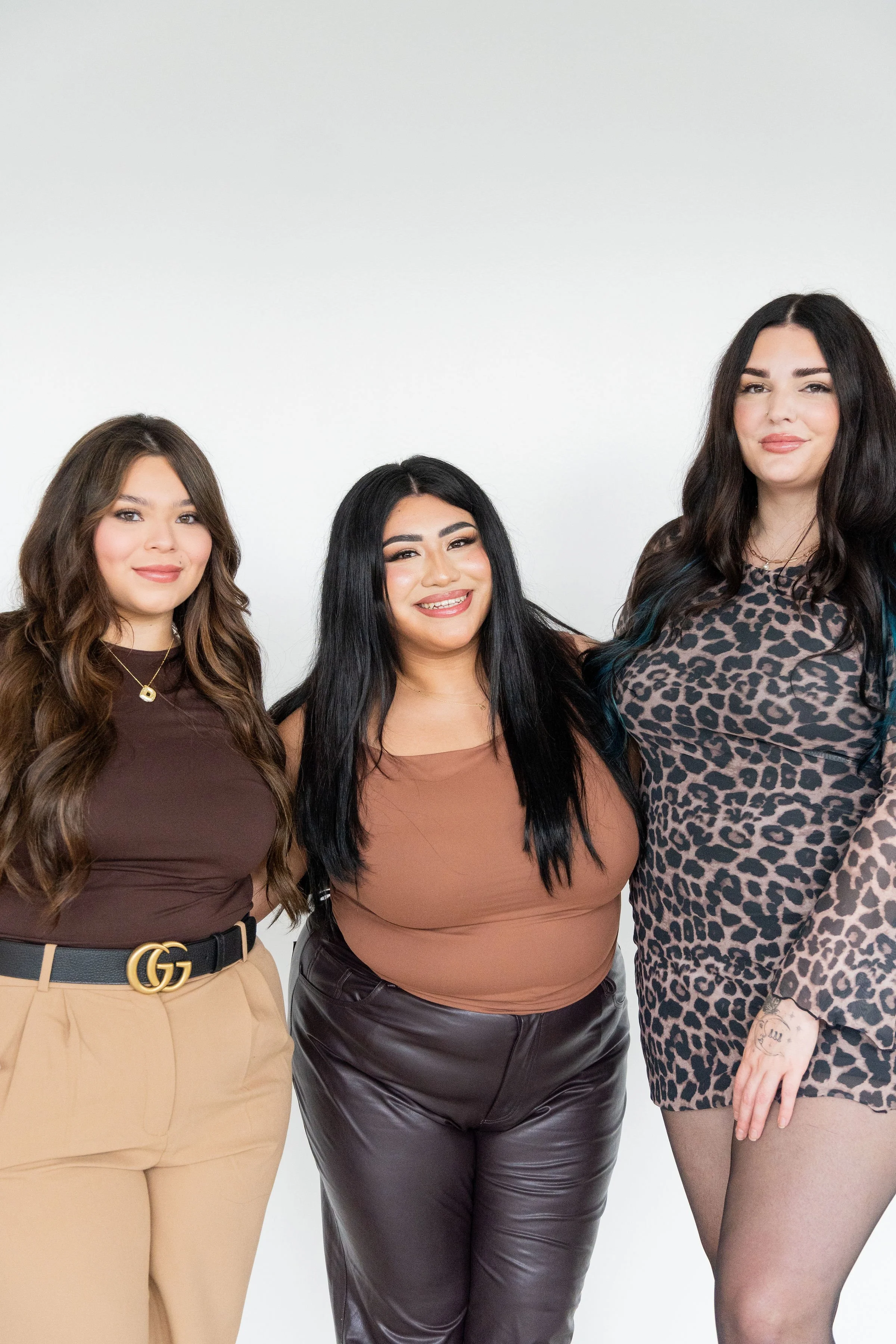 Three women standing together, smiling, against a plain white background.