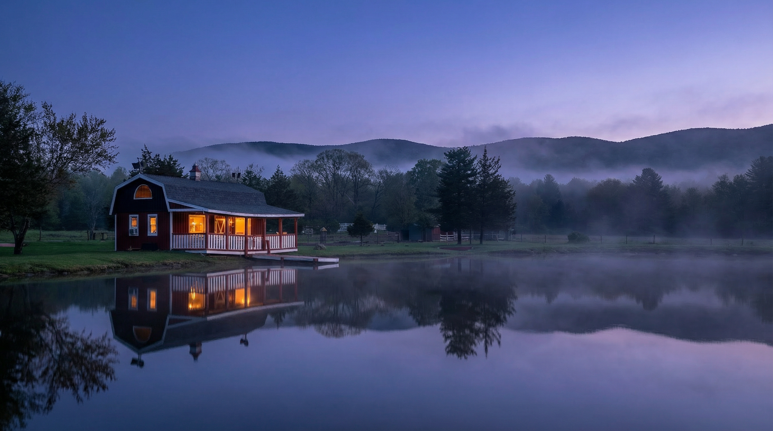 A red cabin with a porch is near a calm lake that reflects the cabin and surrounding trees. The sky is in shades of purple and blue, with mountains and mist in the background.
