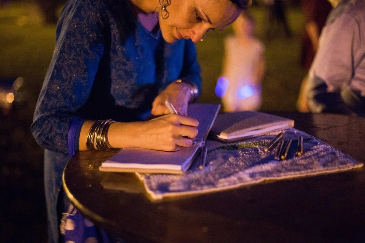 A woman signing a guestbook at an outdoor event during the evening.