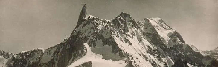 A black and white photograph of a mountain with a sharp peak and snow-covered slopes.