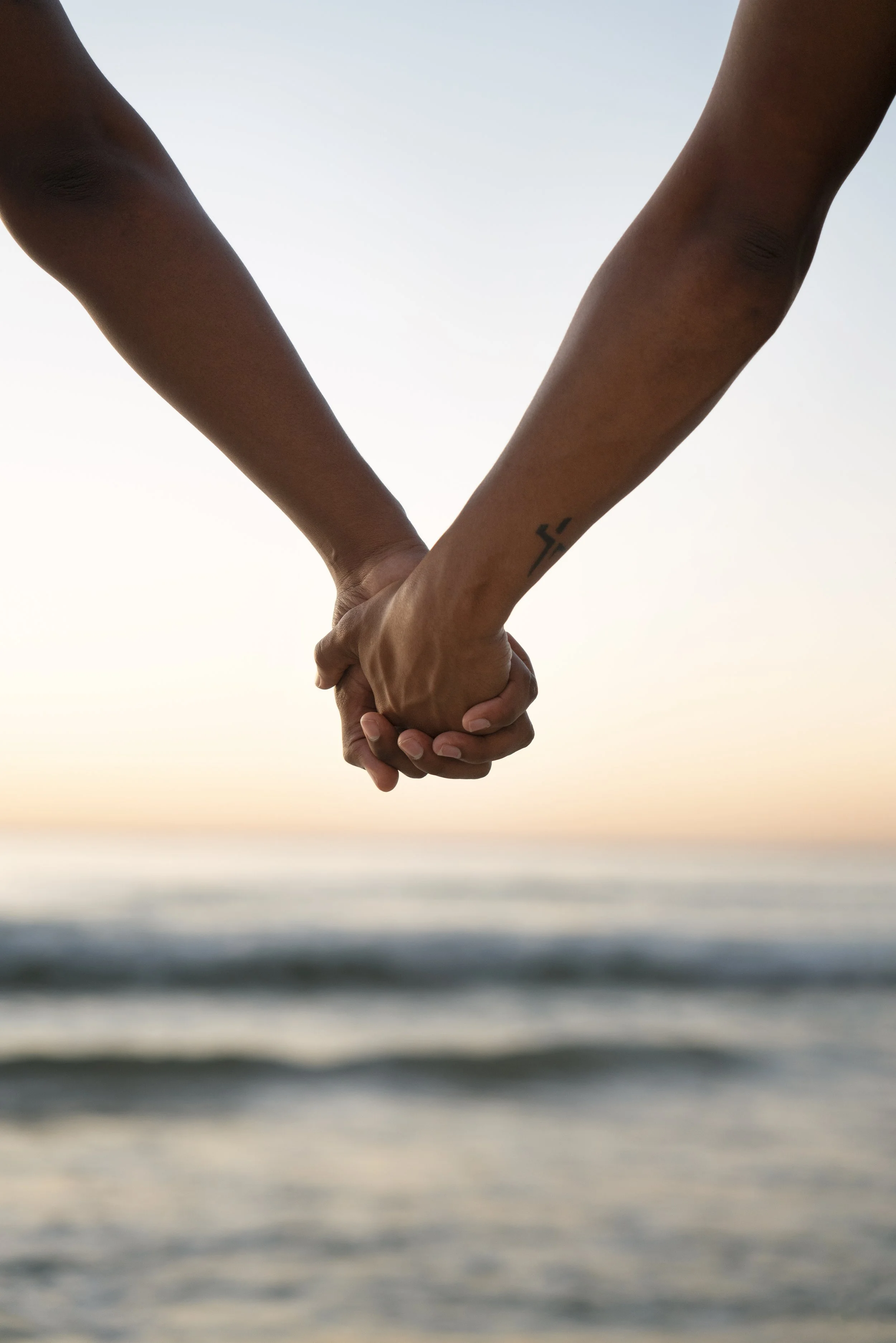 Two people holding hands over a blurred ocean with a sunset sky.