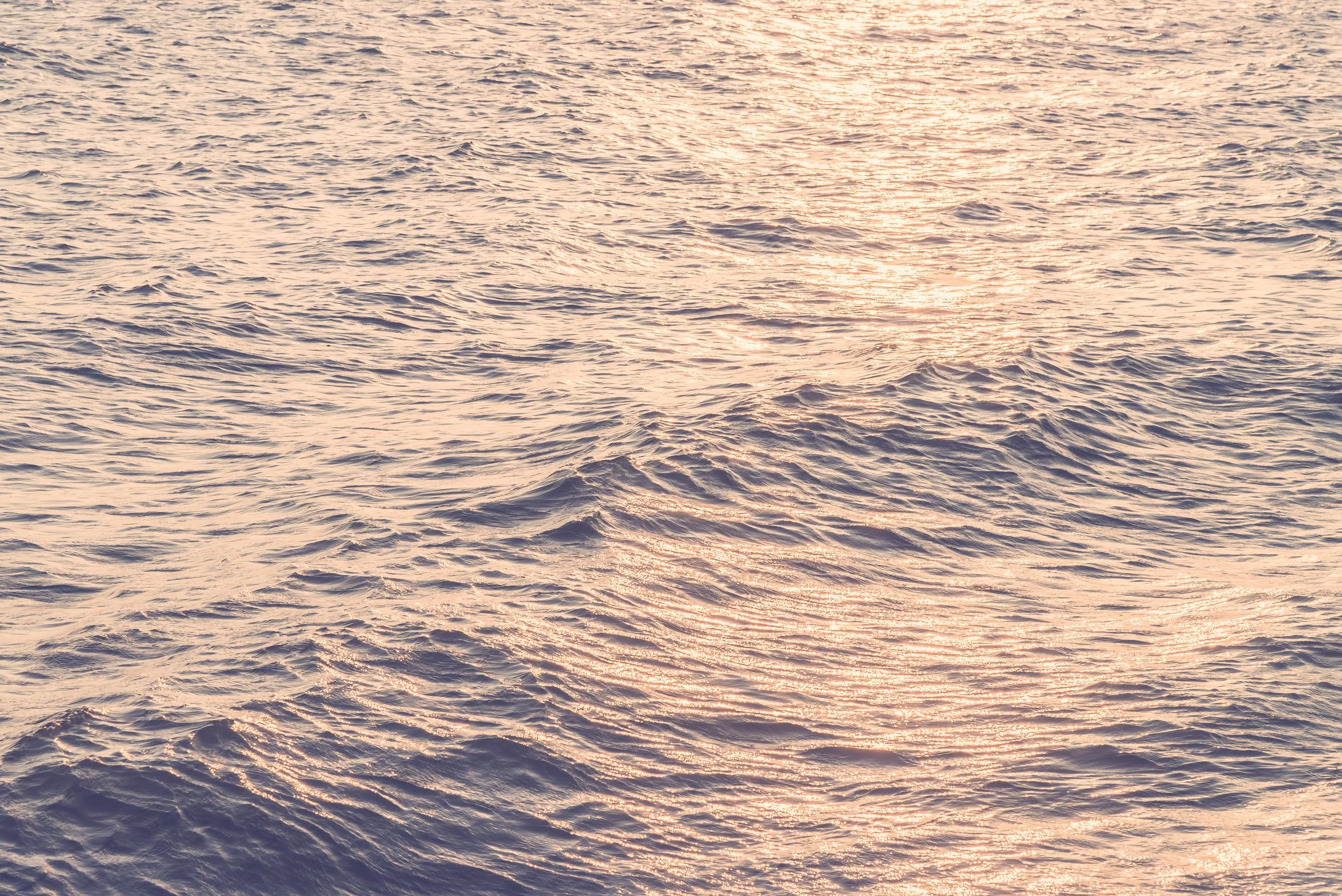 A body of water with gentle waves reflecting the warm colors of a sunset or sunrise.