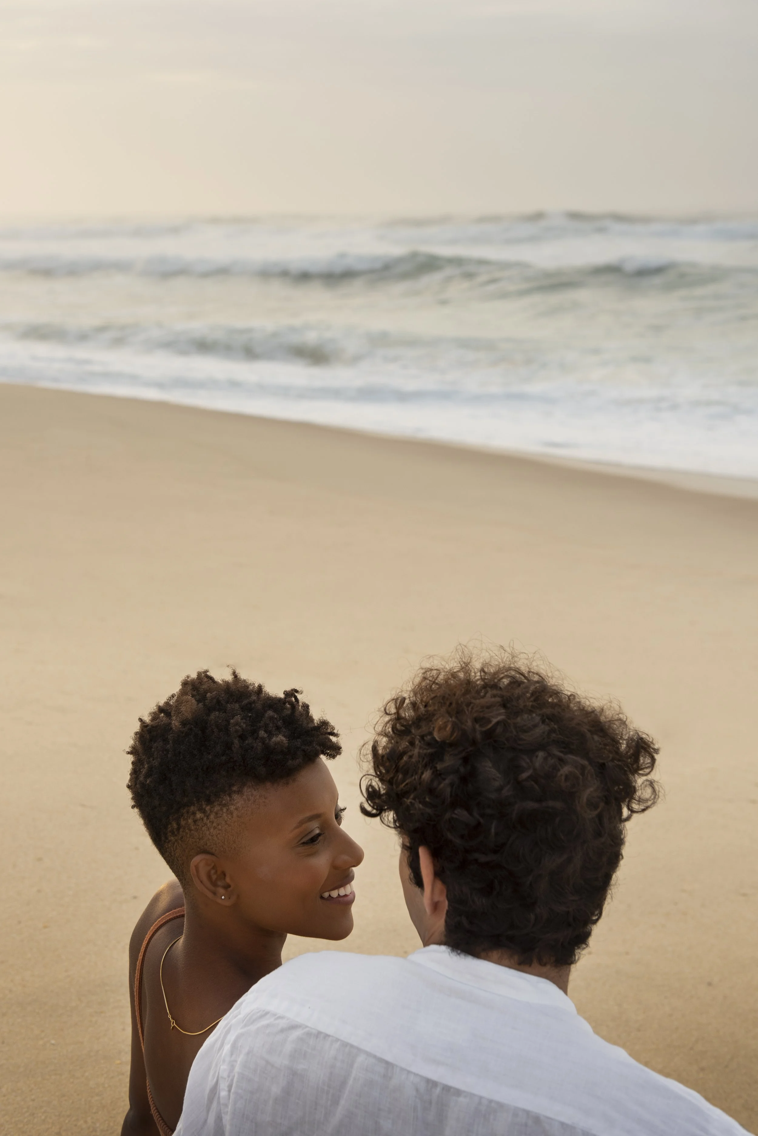 A couple smiling and facing each other on the beach.