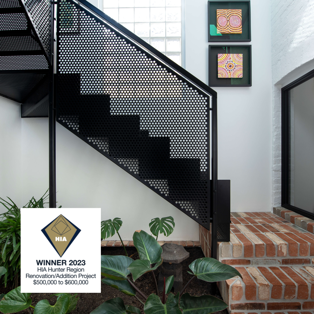 Modern interior staircase with perforated black metal railing, white walls, framed abstract artwork, brick steps, and indoor plants.