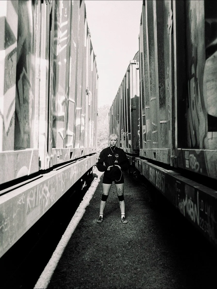 A person standing between two train cars with graffiti on the sides, on a narrow gravel path.