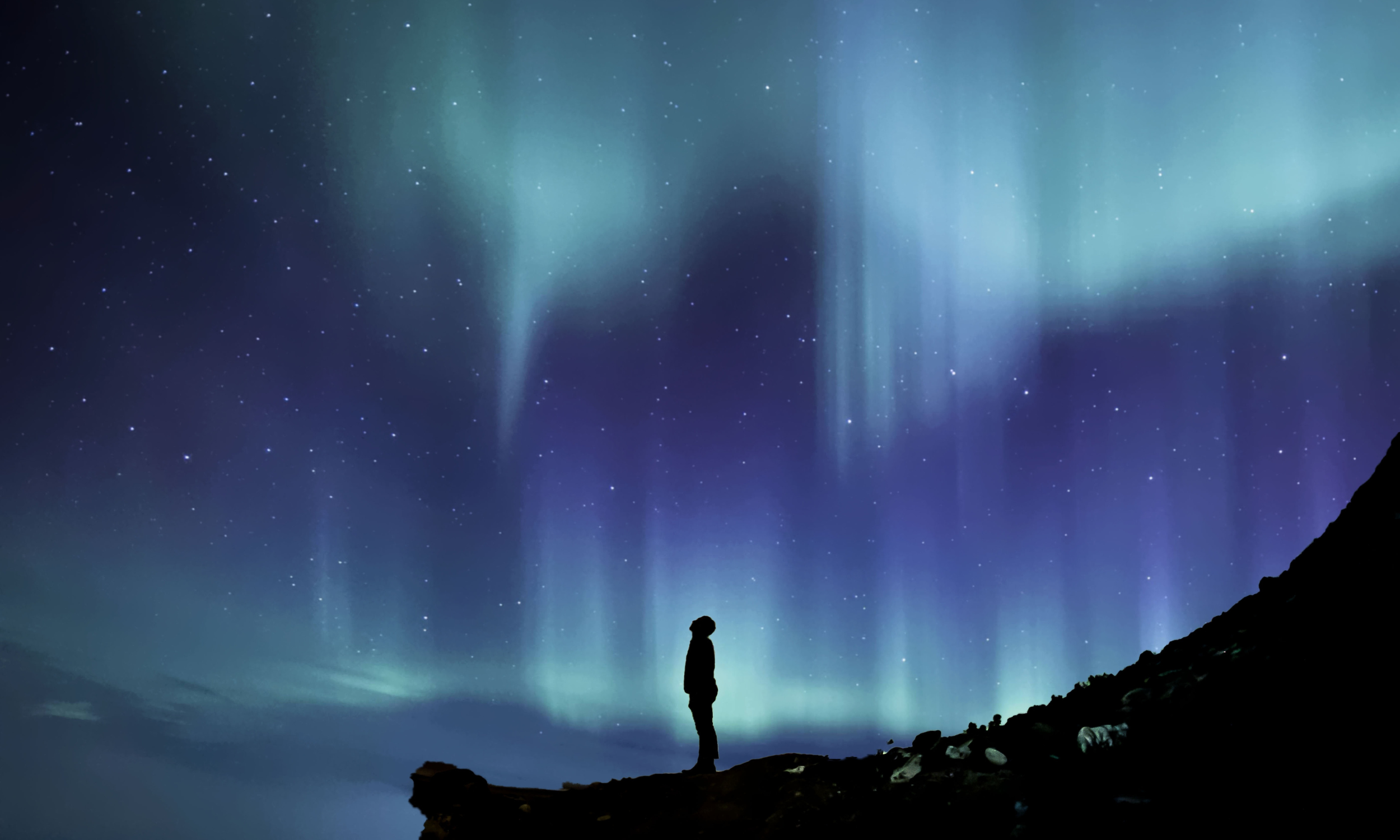 a person looks up in wonder at the Aurora Borealis