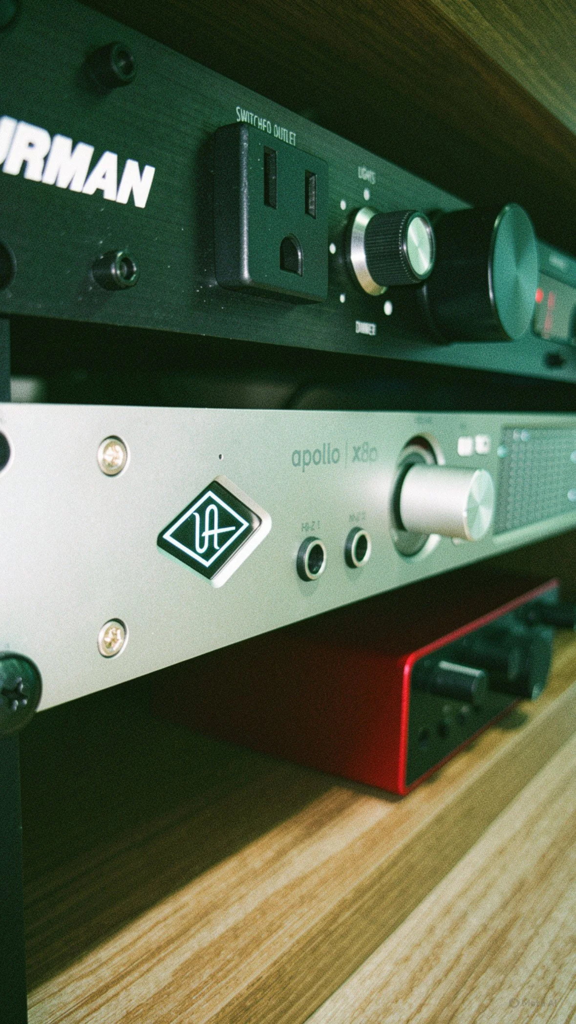 Close-up of audio equipment with a black switcher, a silver knob, and logos, placed on a wooden shelf.