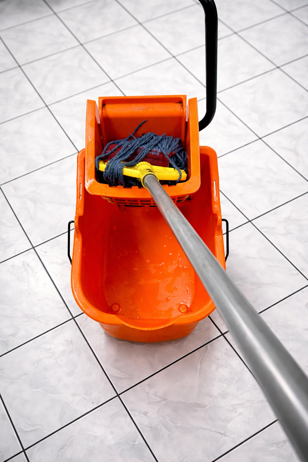 Orange mop bucket with mop head inside, on a tiled floor.
