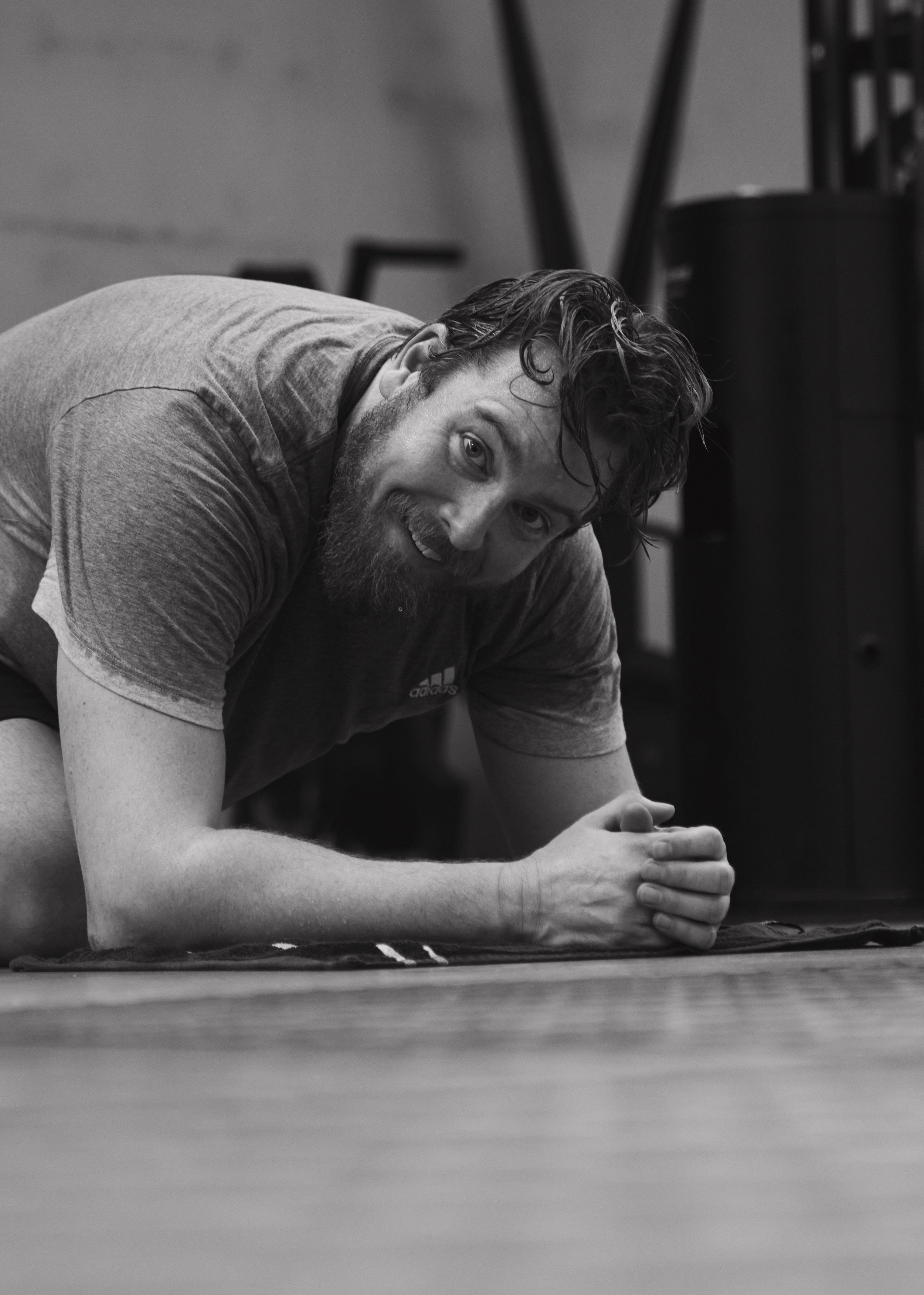 A man with a beard and wet hair doing a plank exercise on a yoga mat in a gym.