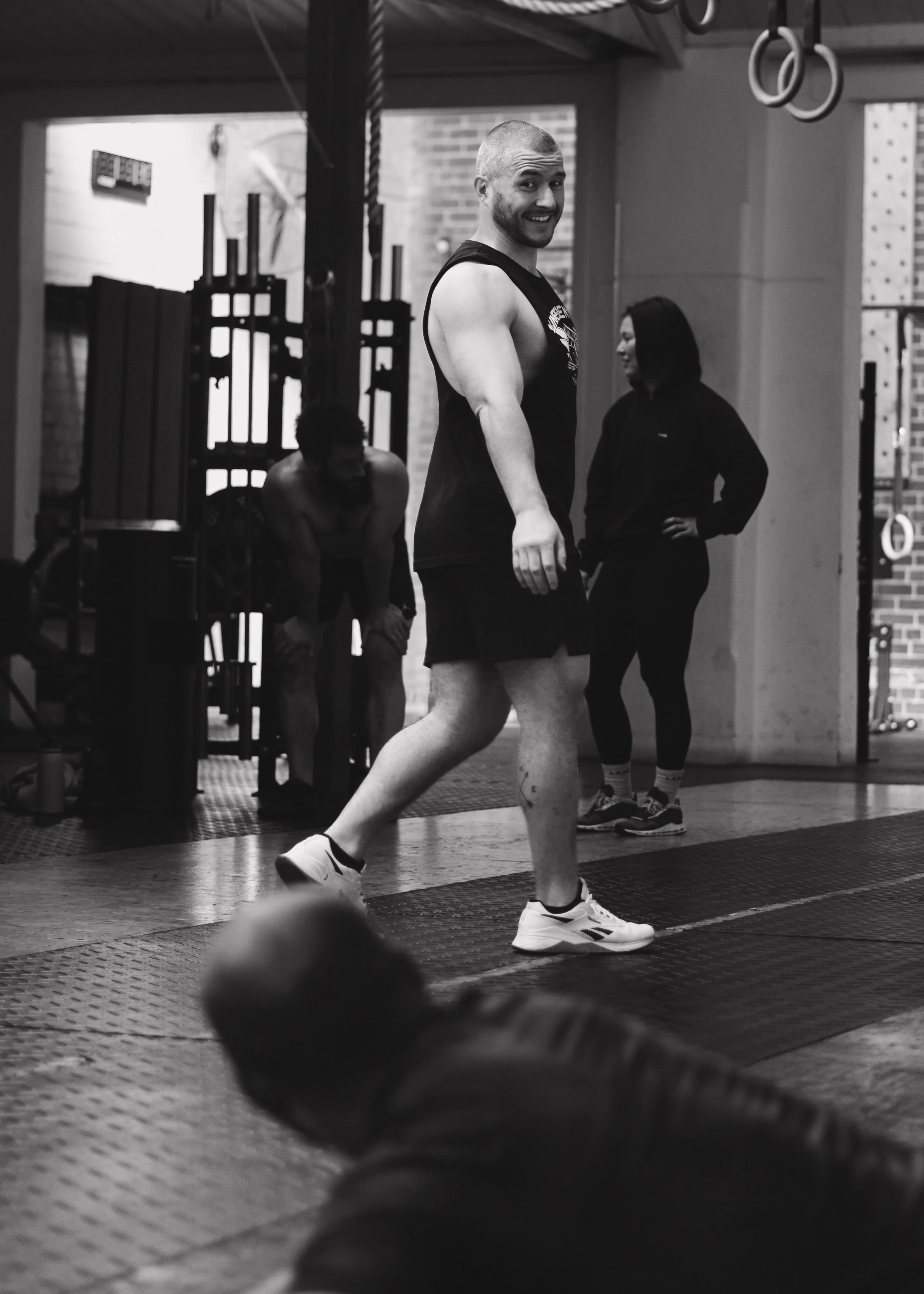 A man smiling at the gym, with other people working out in the background.
