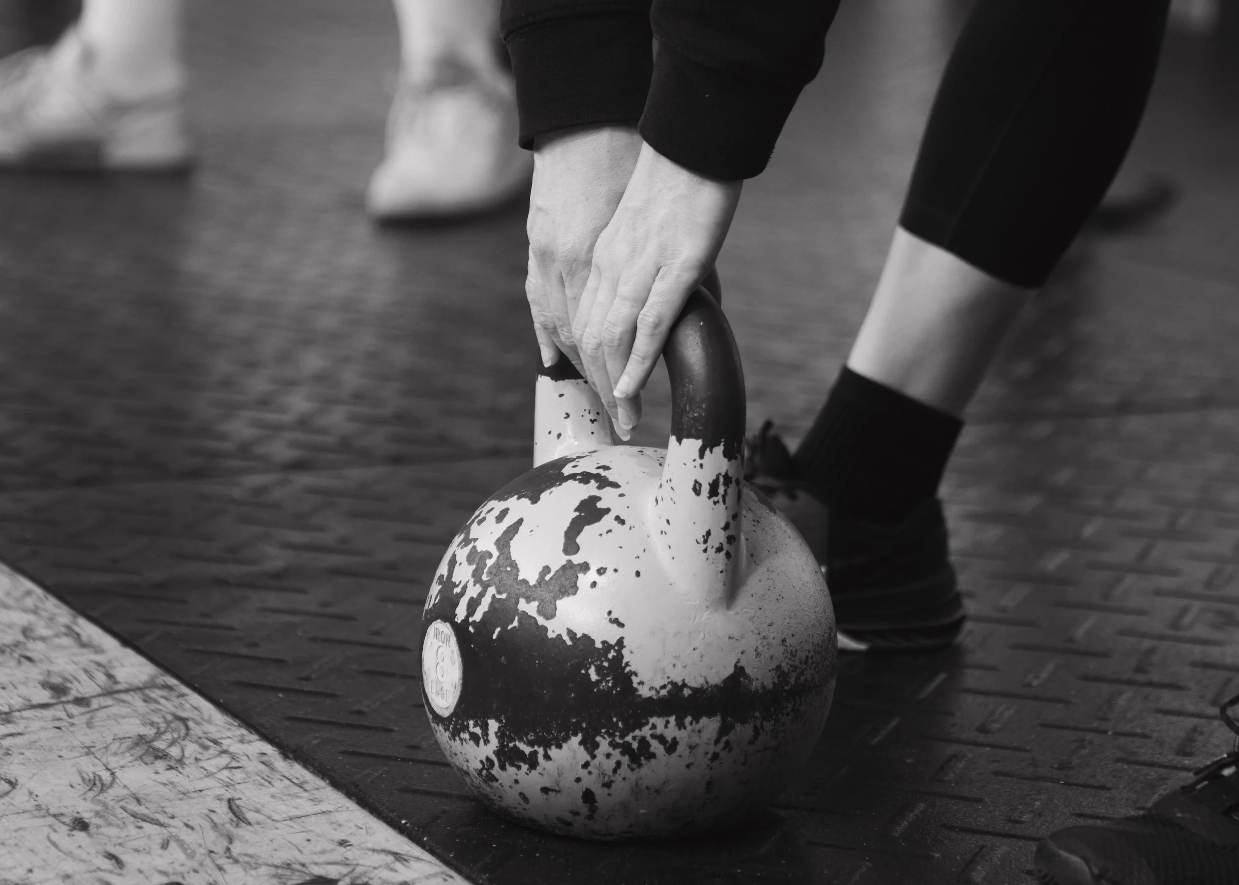 Someone lifting a kettlebell during a workout, with other gym equipment visible in the background.