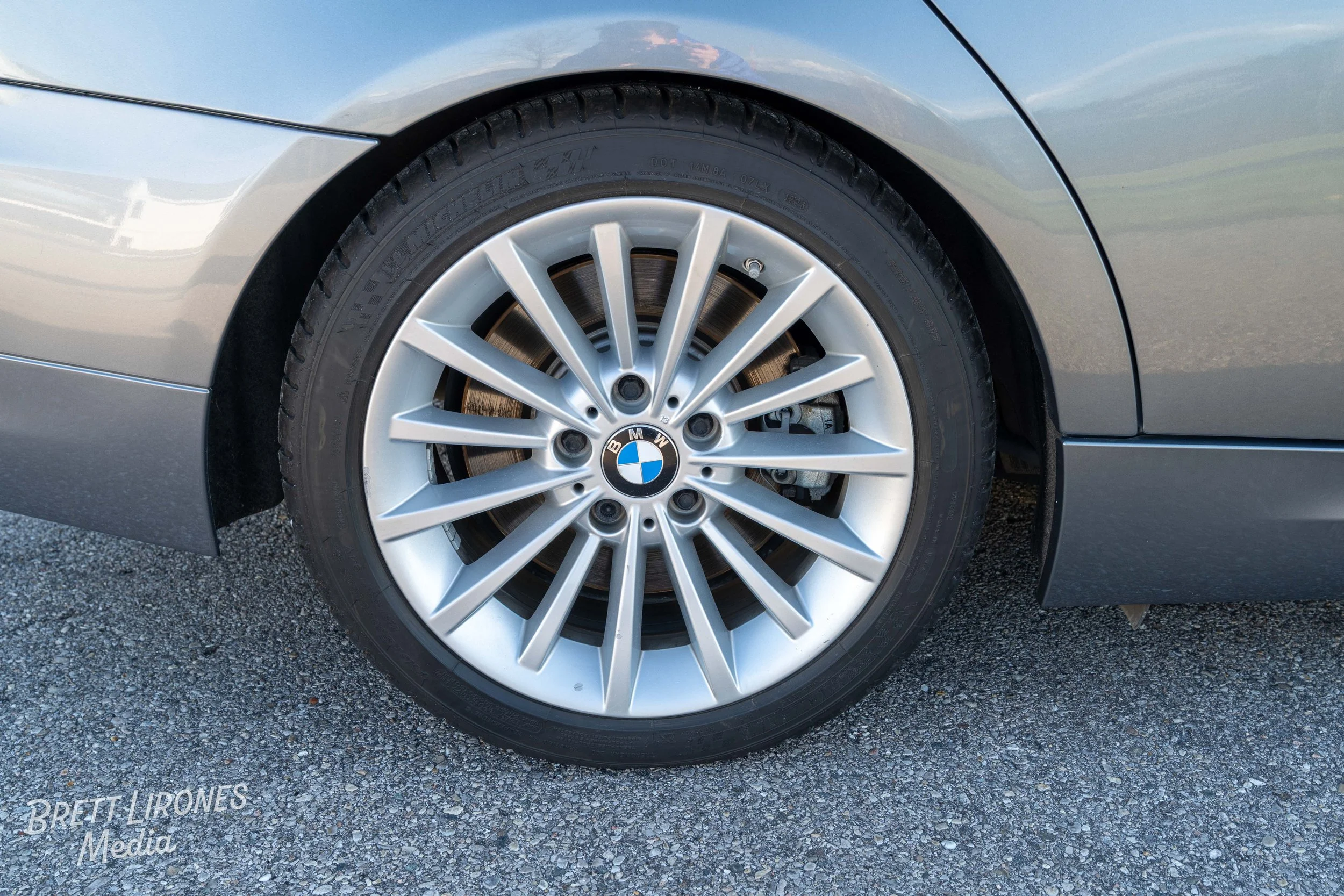Close-up of a silver BMW car wheel with a Bridgestone tire, parked on asphalt.