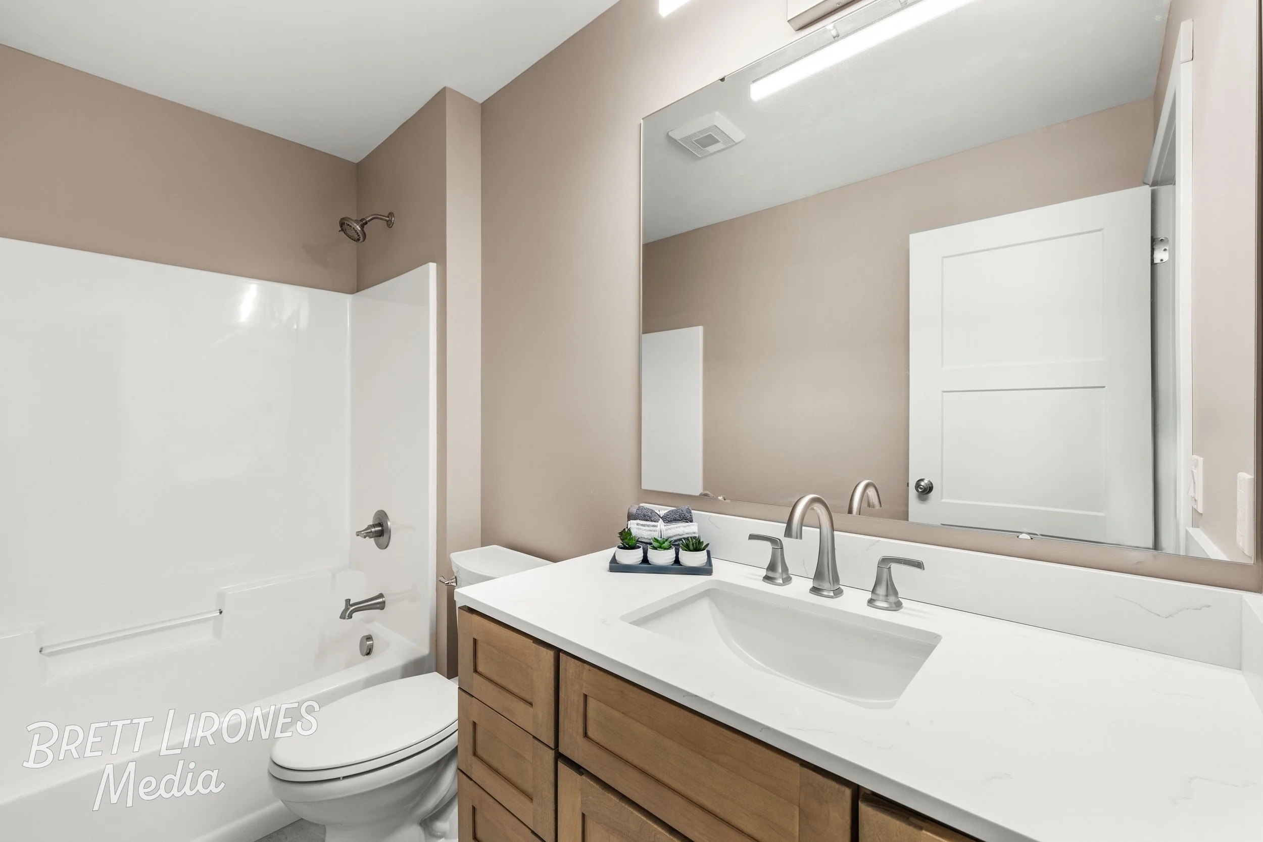 Bathroom with a white bathtub, beige walls, a wooden vanity with a white countertop, a large mirror, and a closed white door.