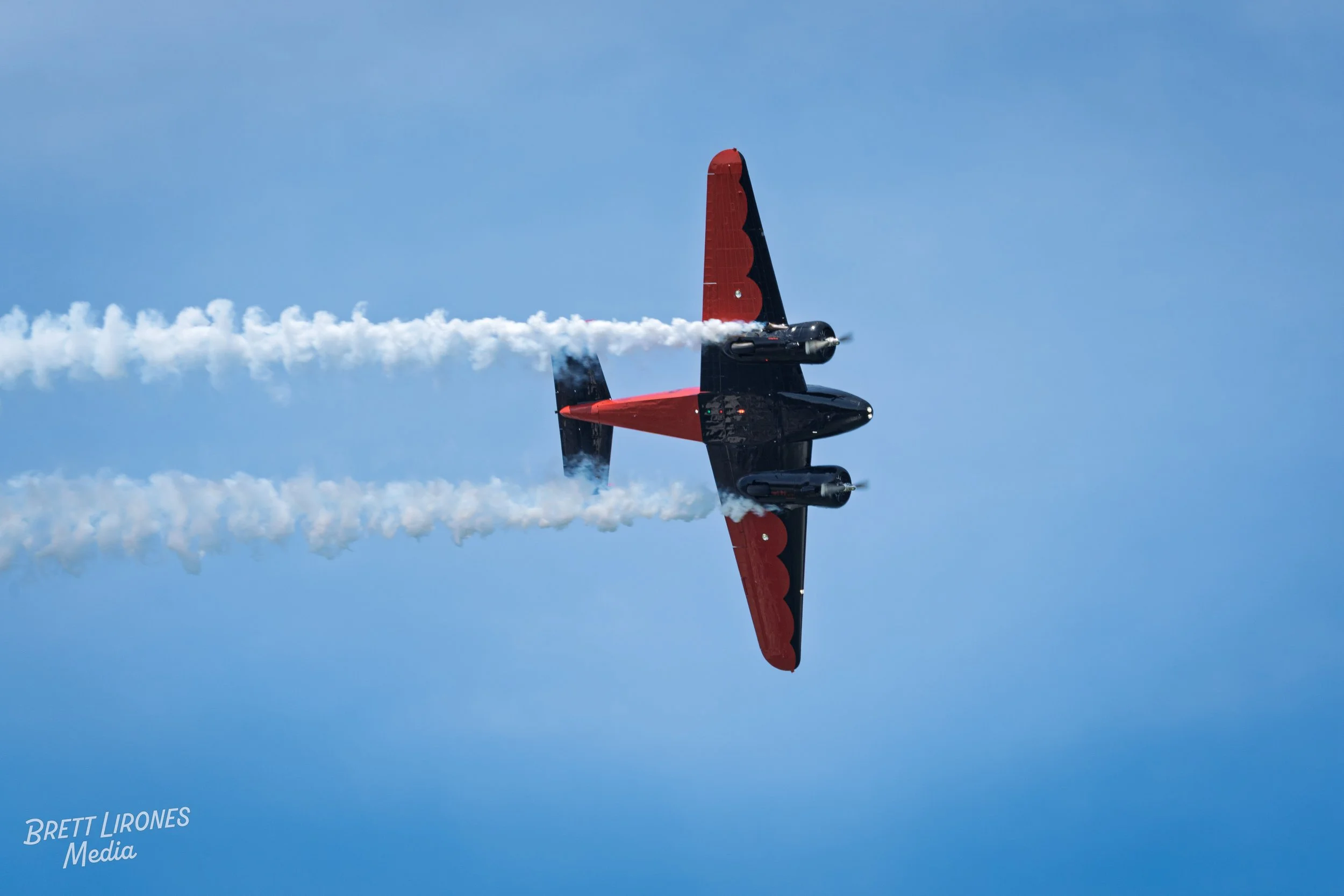 A black and red aerobatic airplane performing a stunt in the sky, leaving white smoke trails behind.