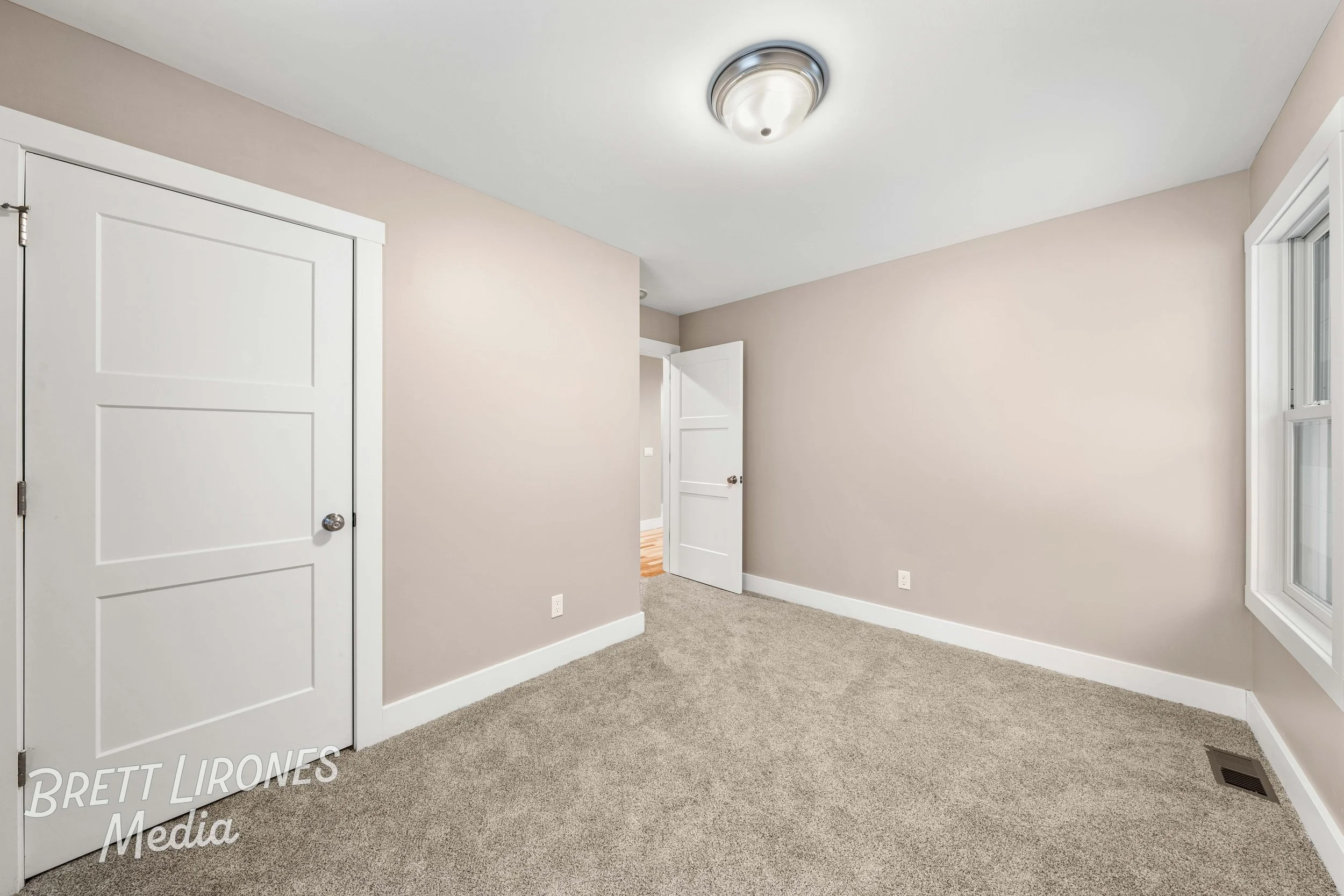 Empty bedroom with beige walls, white trim, tan carpet, and two windows on the right side.