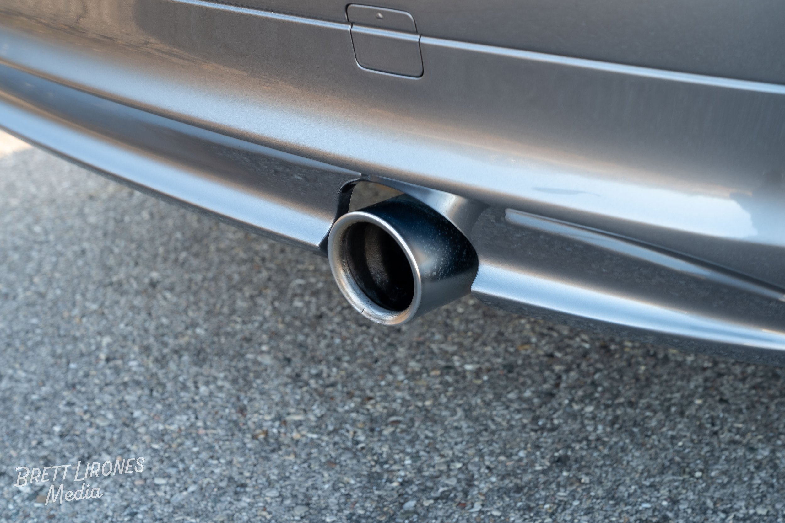Close-up of a car's exhaust pipe on a gray vehicle parked on pavement.