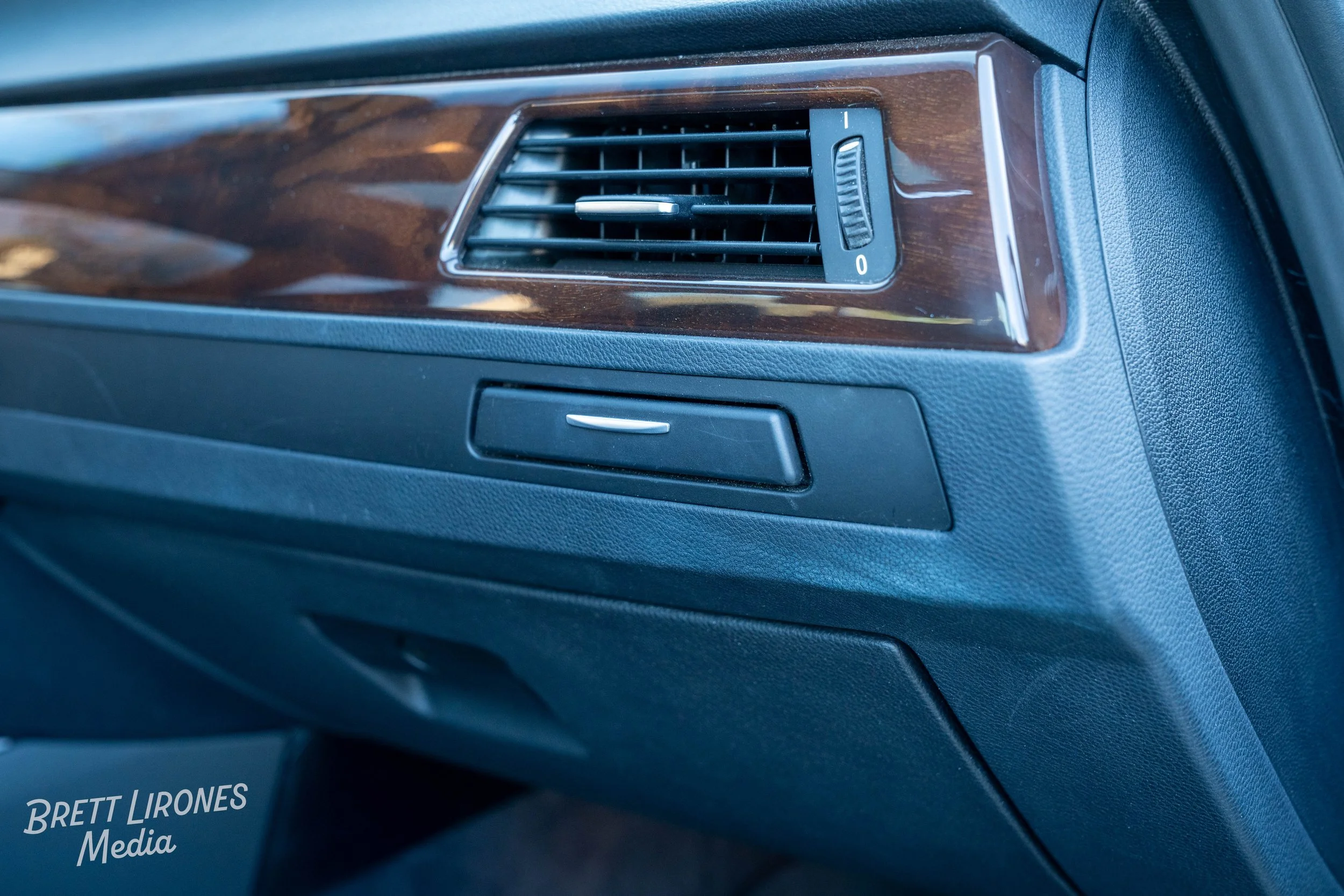 Close-up of a car dashboard vent with a wood grain finish and control button beneath it.