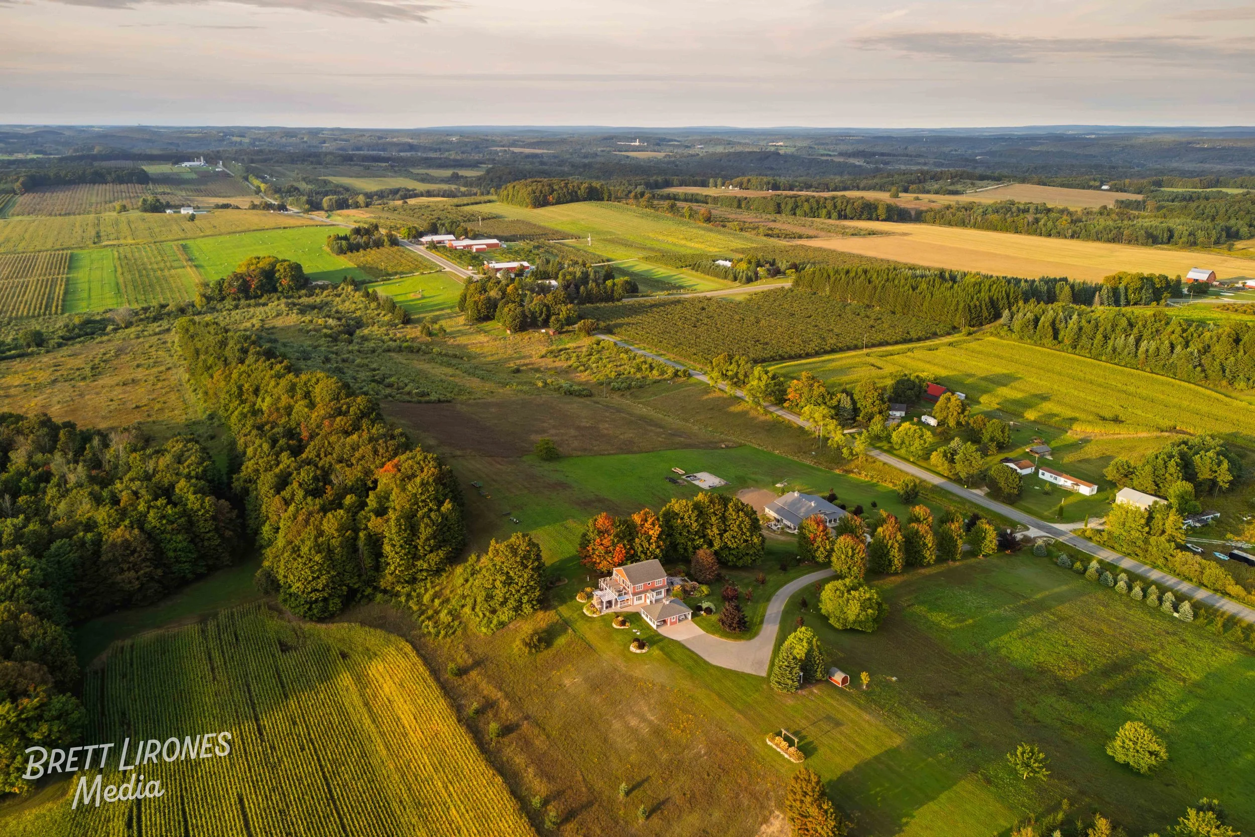 Aerial view of a rural landscape with farmland, trees, a house with a driveway, and fields during the daytime.