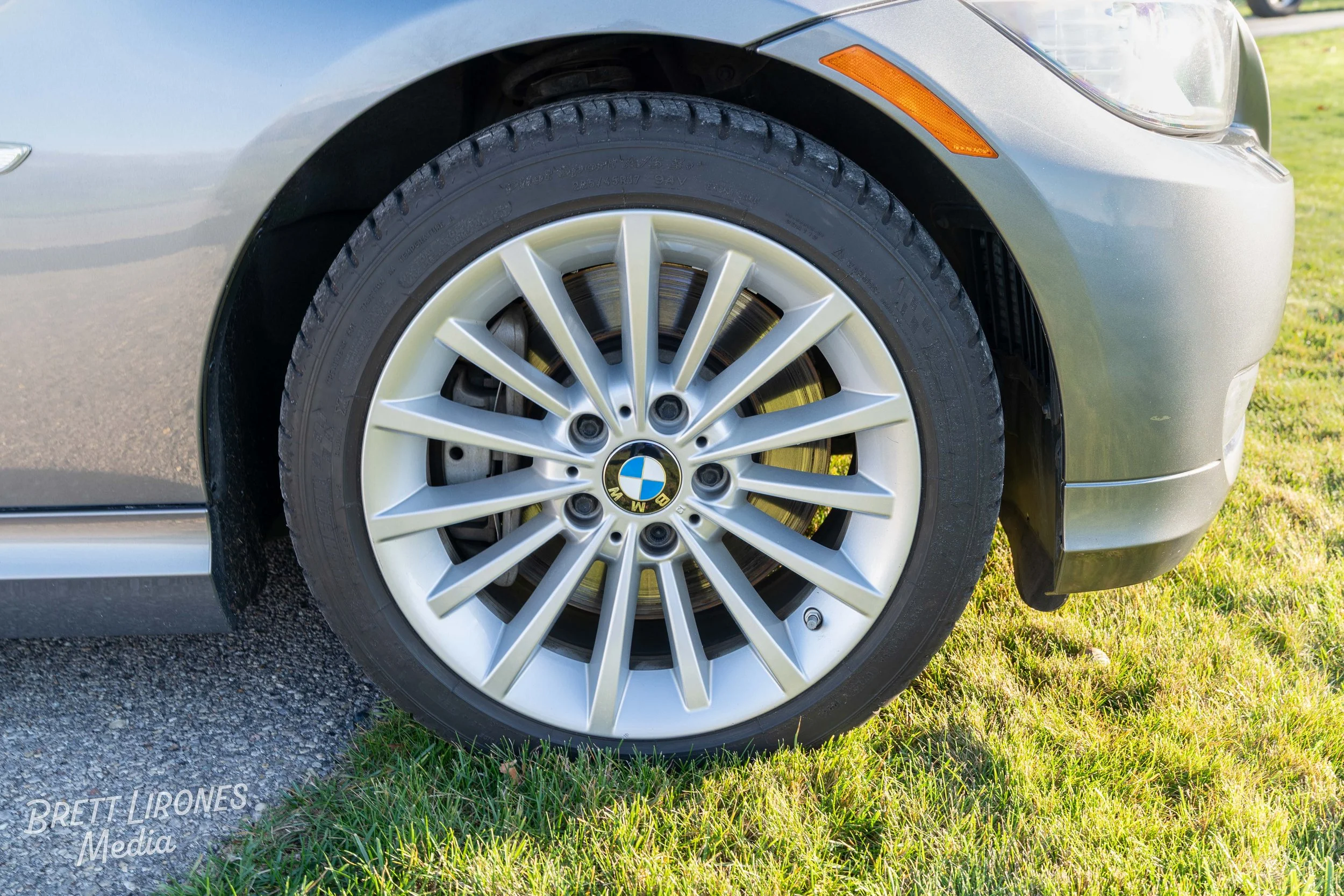 Close-up of a BMW car front tire and alloy wheel on grass and pavement.
