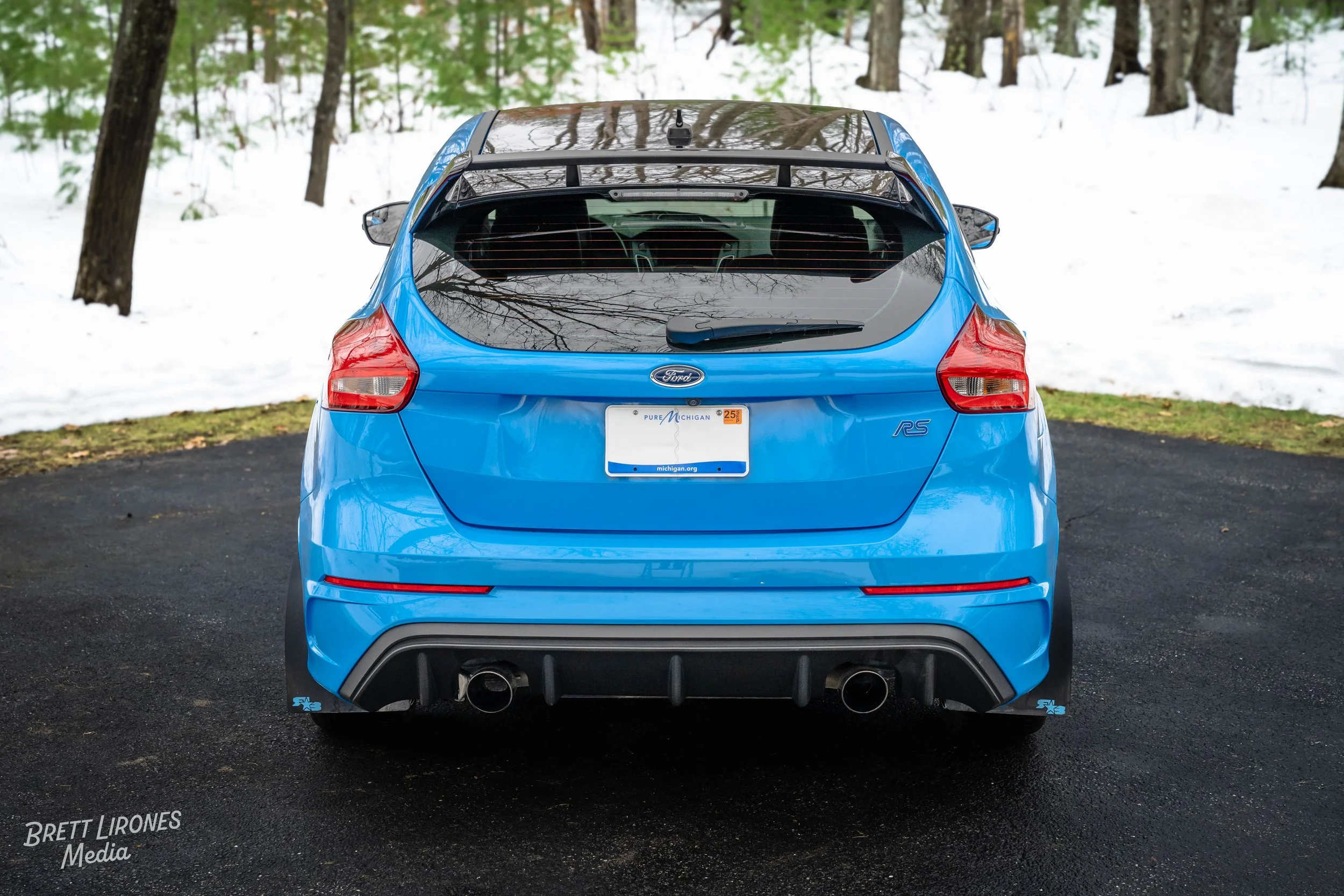 Blue Ford RS hatchback car parked on a paved surface with snow and trees in the background.