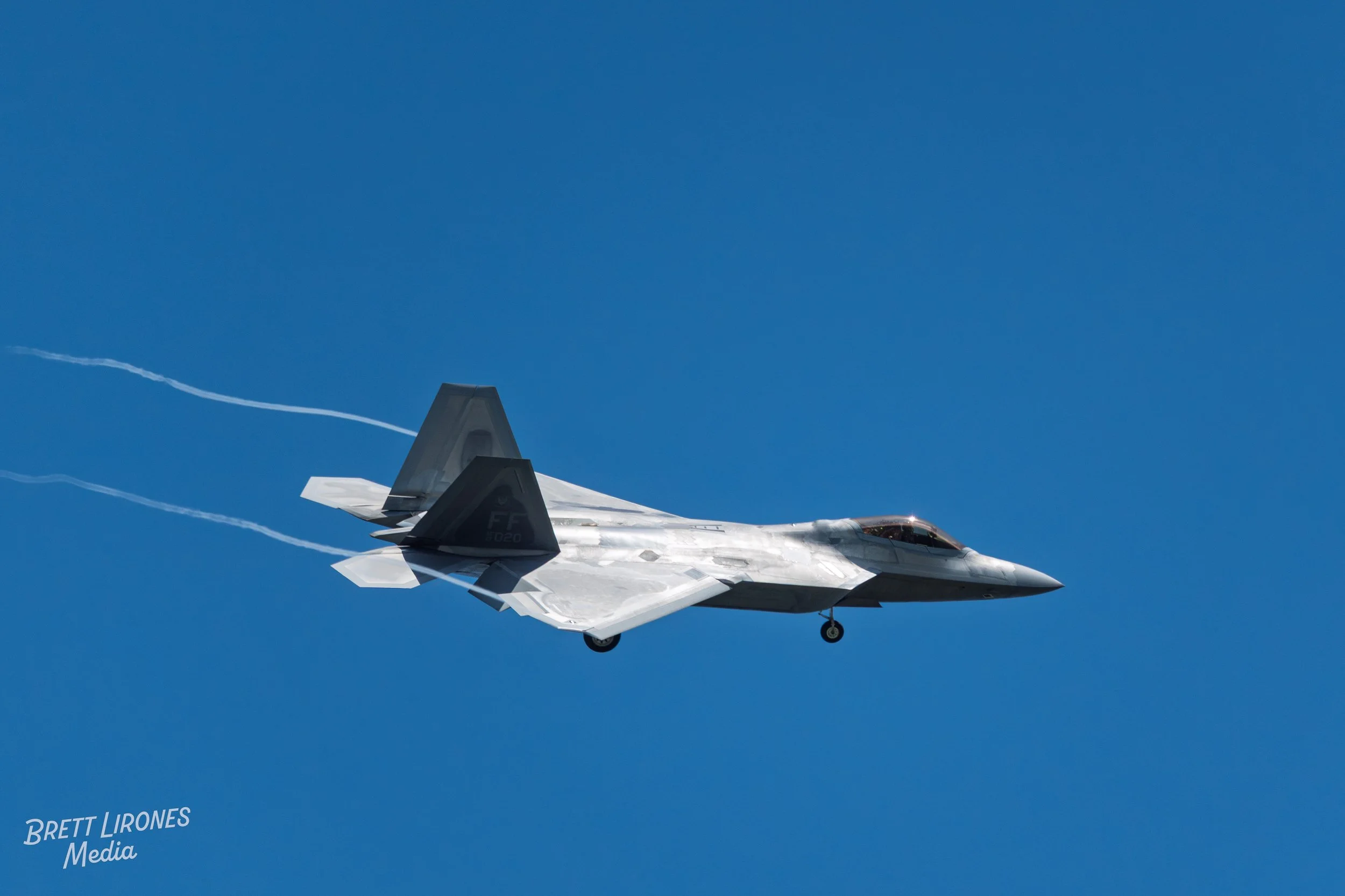 A fighter jet flying in a clear blue sky, leaving white contrail trails behind.